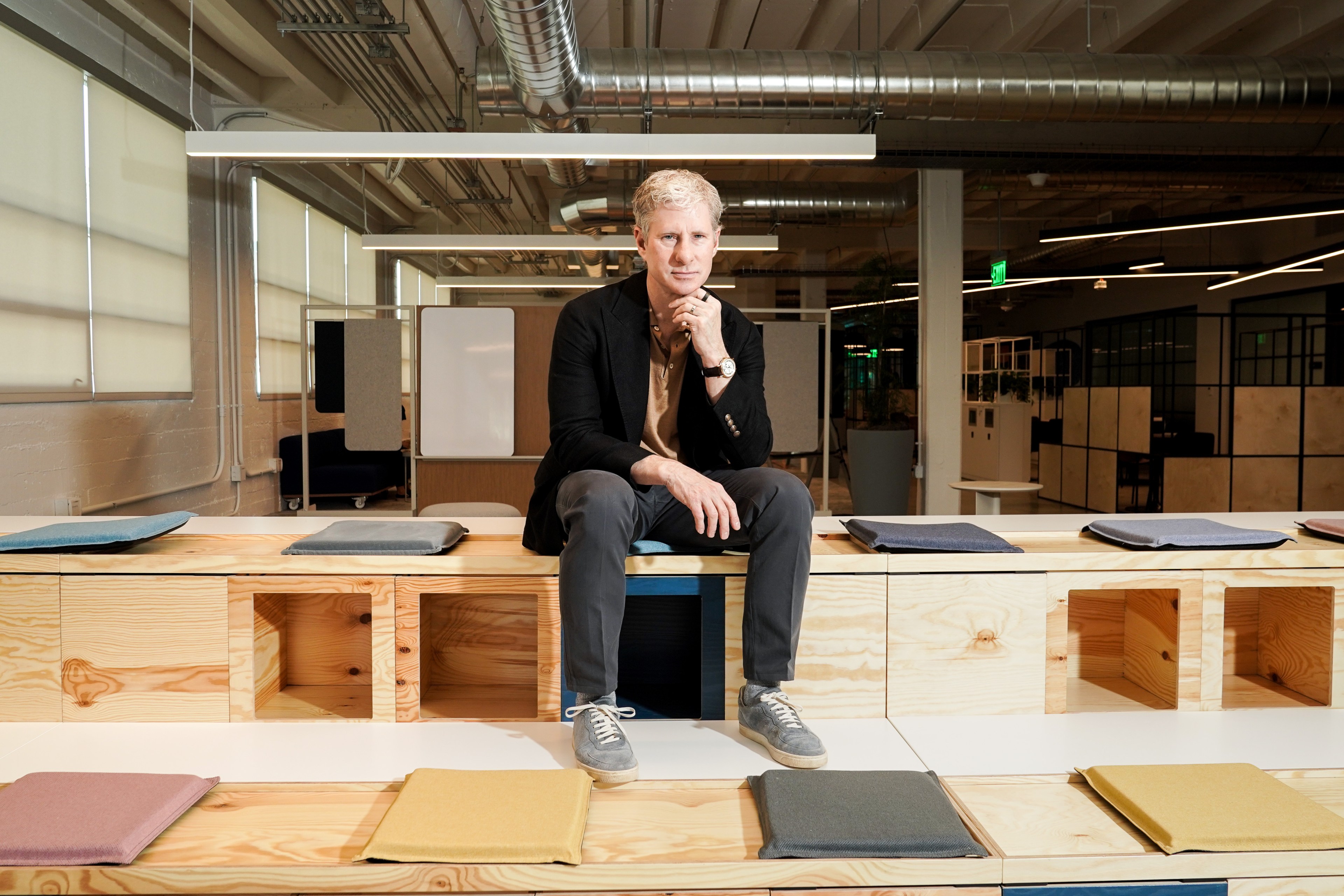Chris Larsen sits on a modular wooden bench in Ripple Labs’ office while surrounded by colorful cushions.
