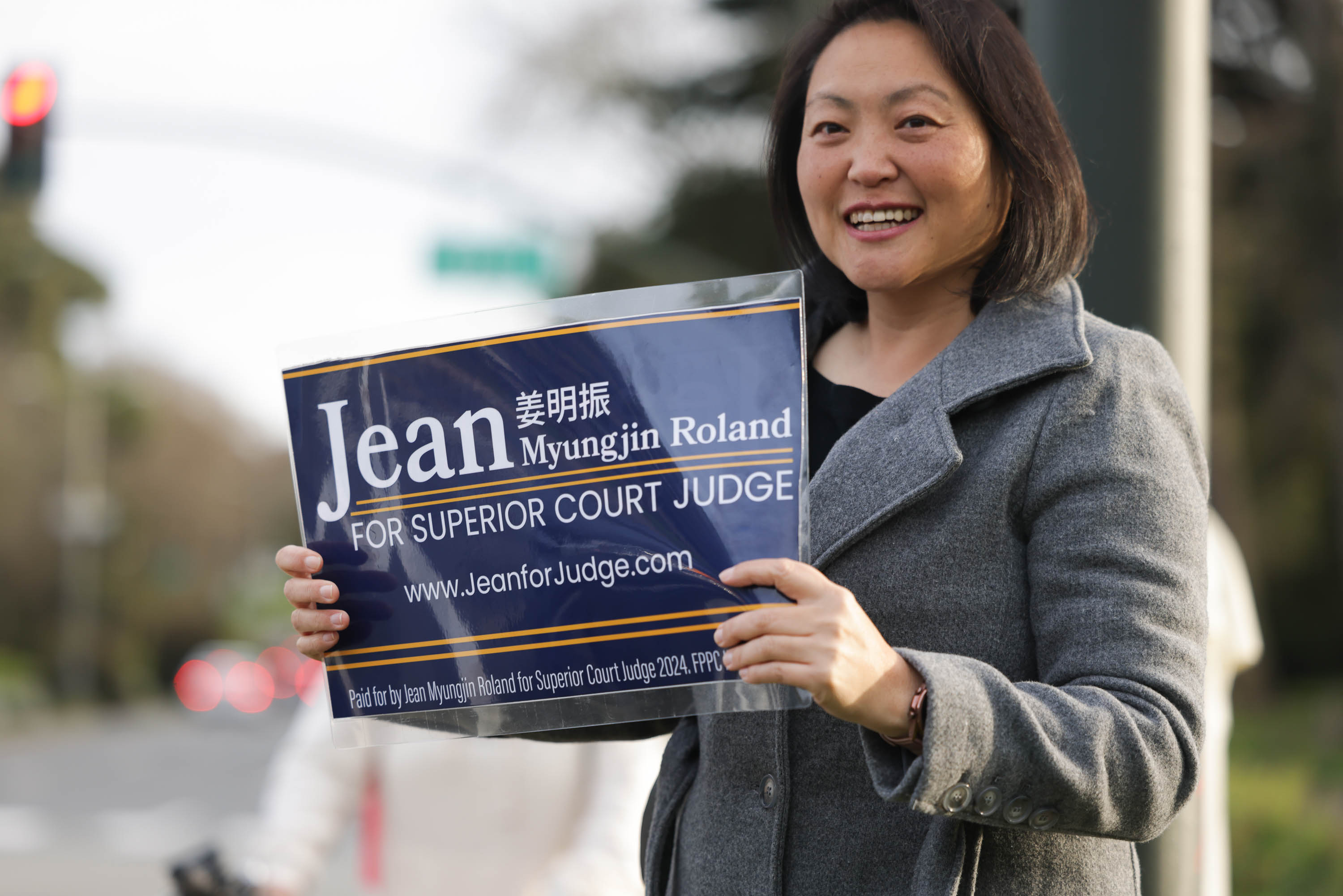 A smiling woman holds a campaign sign for a judicial candidate.