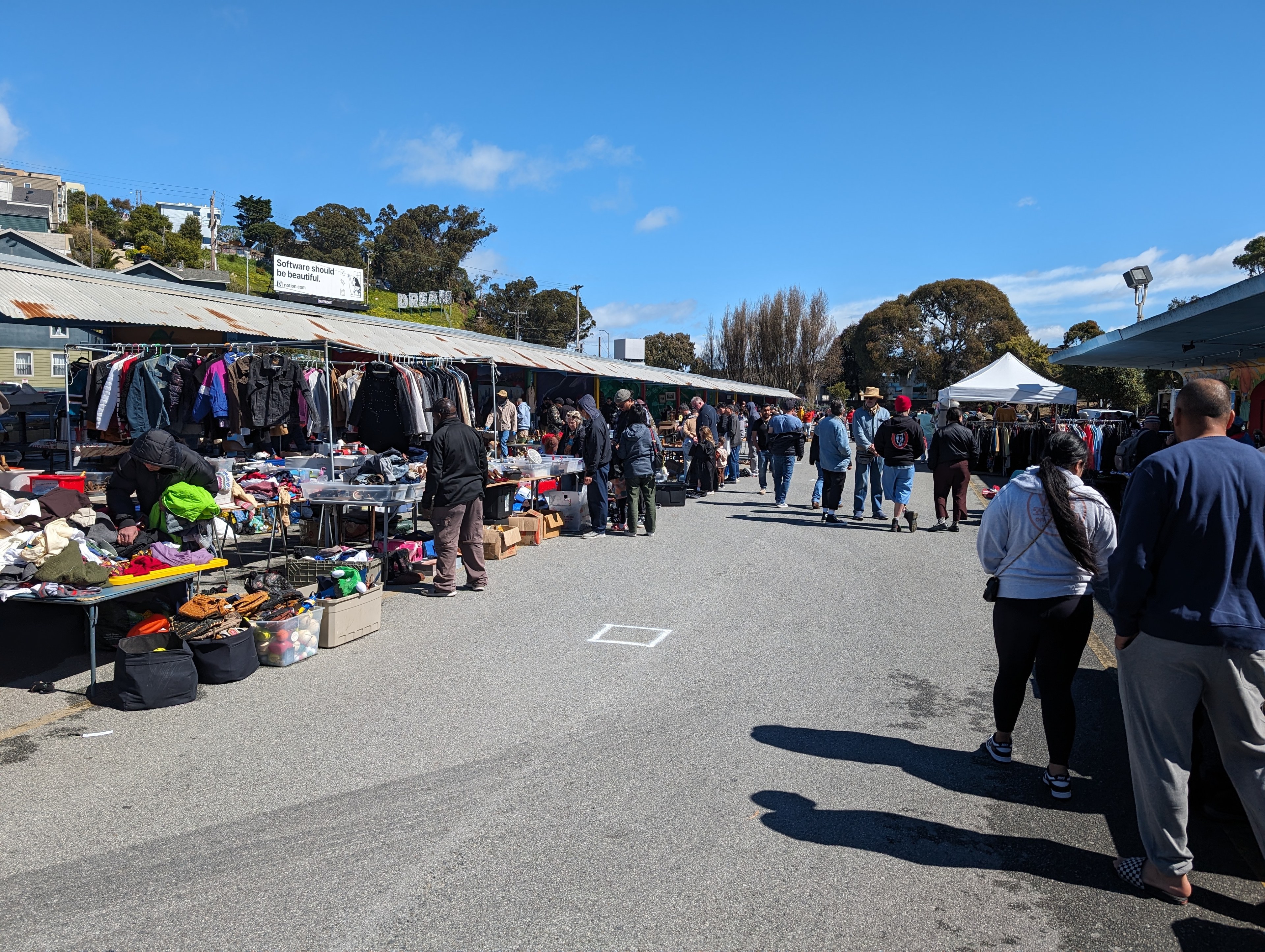 Rows of booths with baskets of clothing and goods await customers at an outdoor flea market.