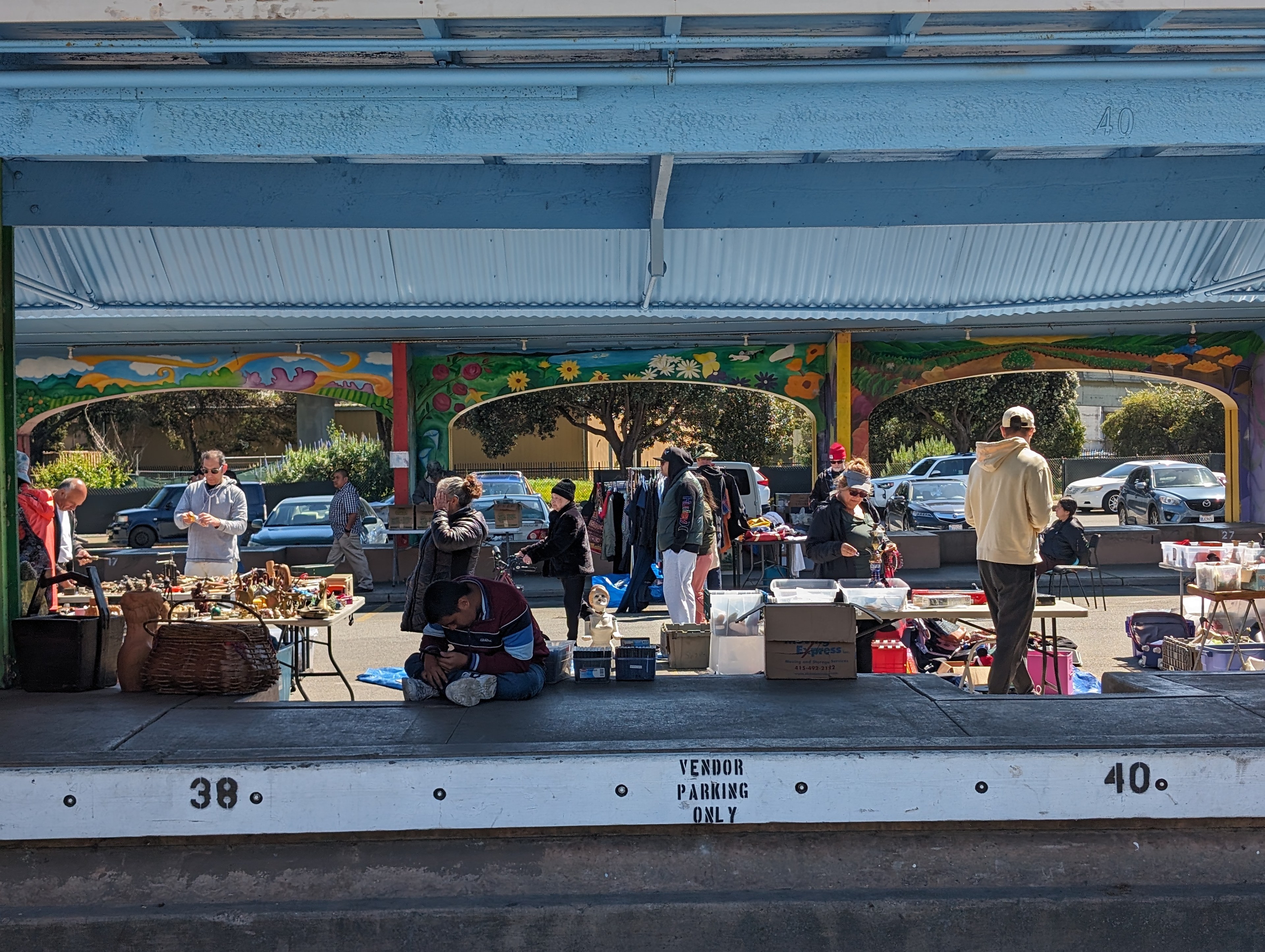 Vendors sell goods at a farmers market parking lot in sunshine.