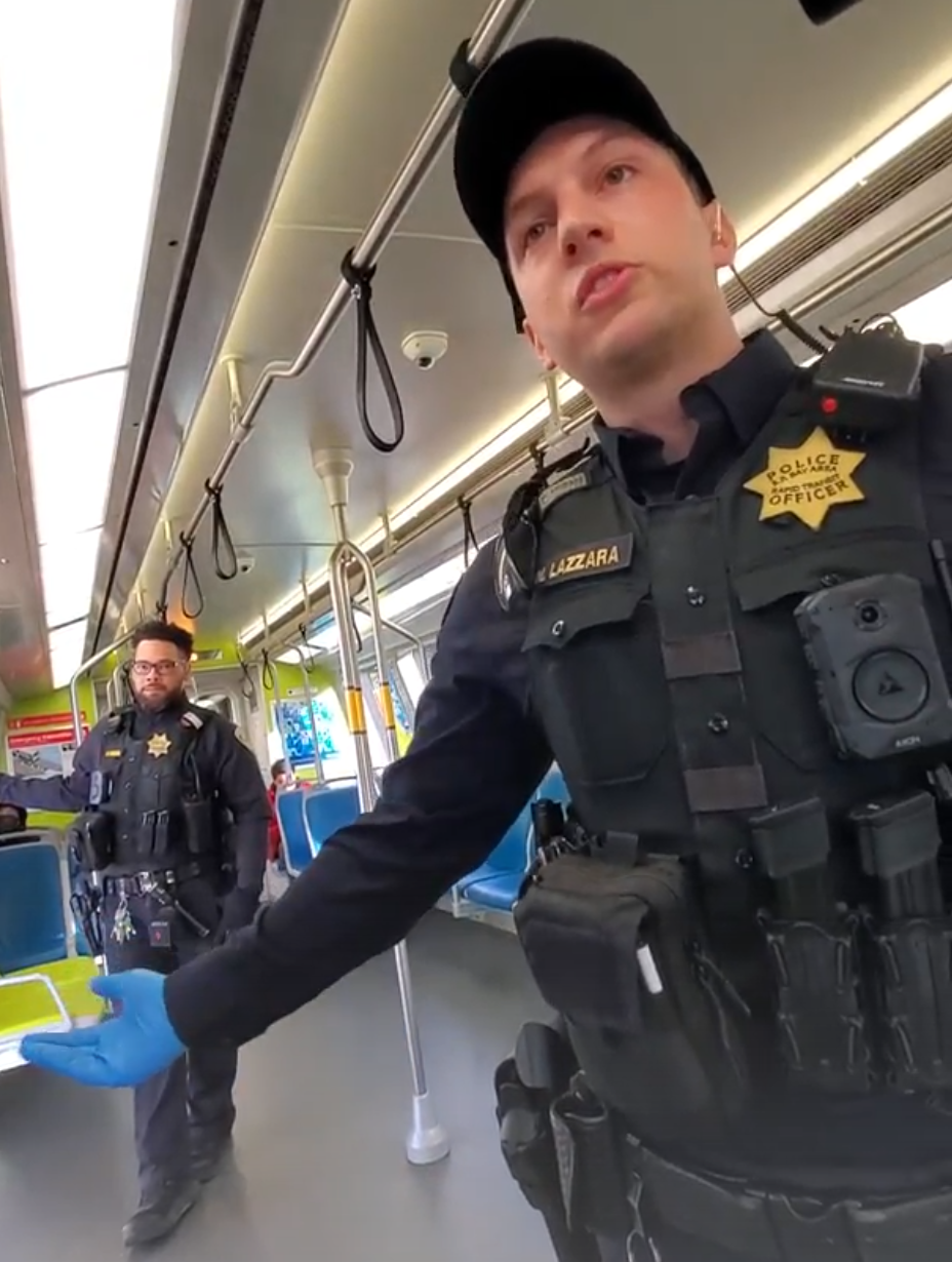 Two police officers speak to a rider on public transit.