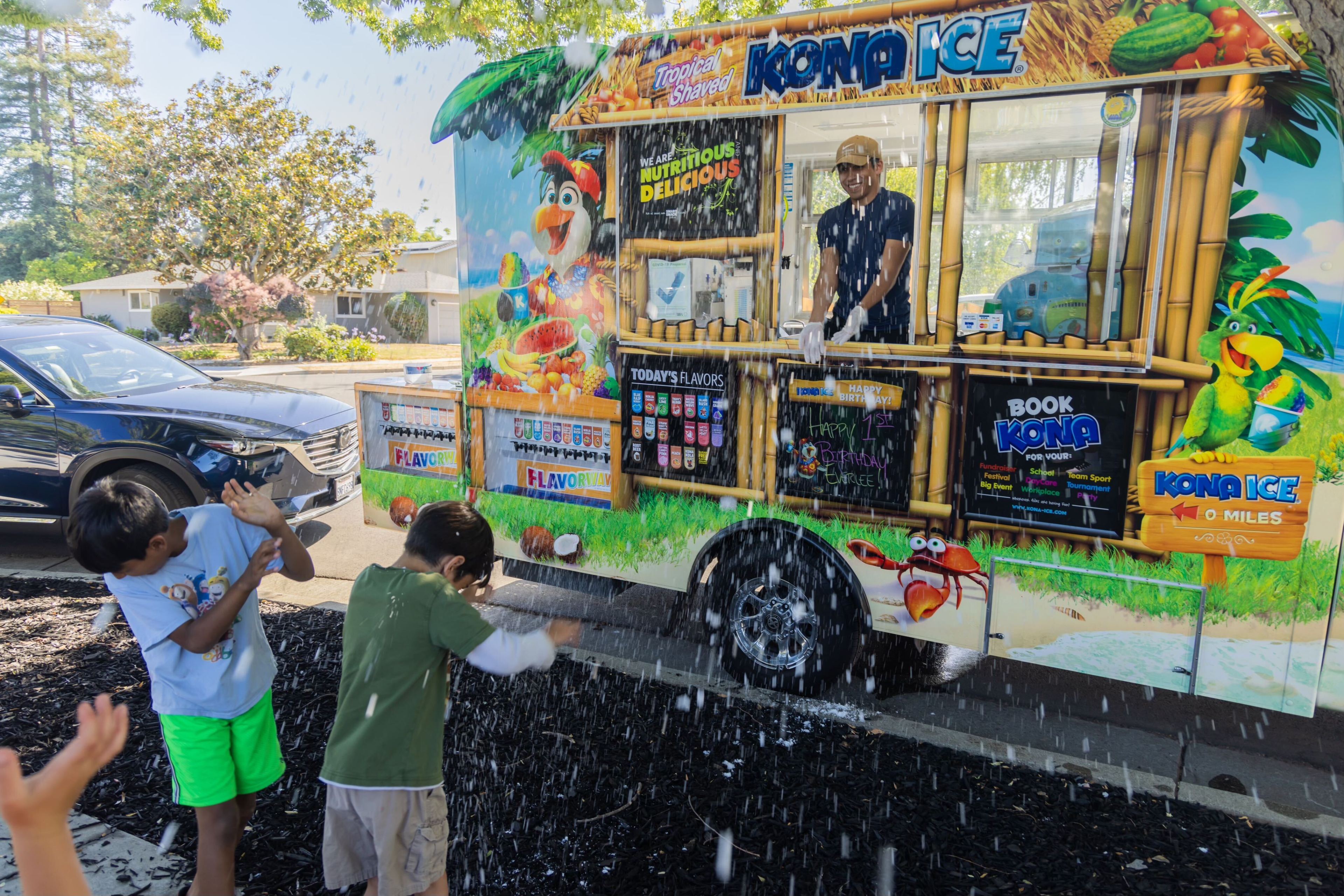A smiling worker in a food truck showers children with stray shaved ice on a warm summer day