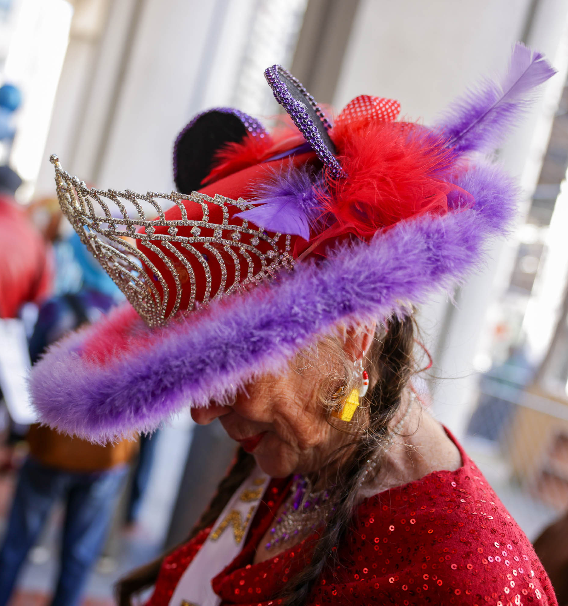 A person in a colorful, feathered hat and sequined red top. The mood suggests a festive or carnival atmosphere.