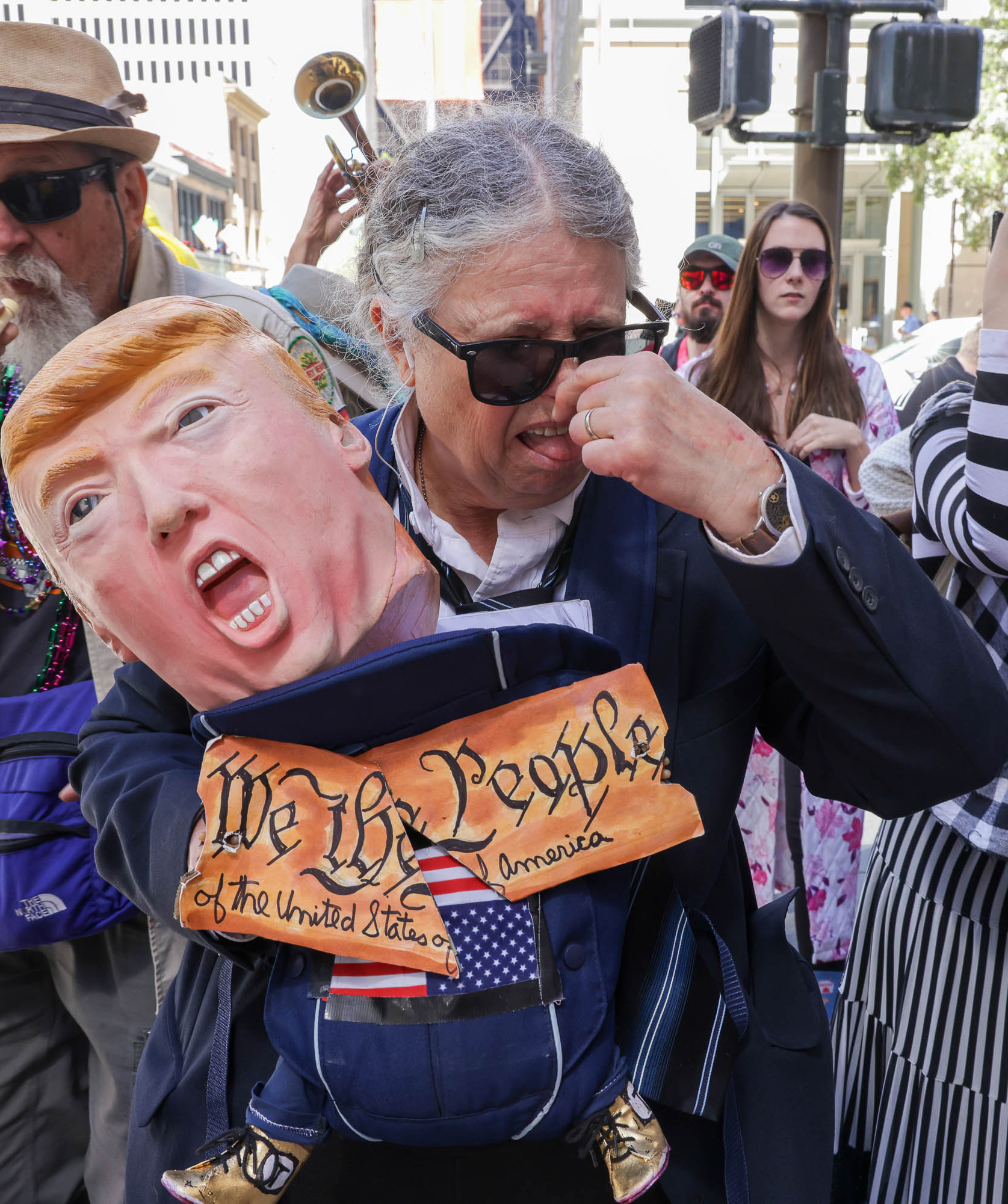 A person is holding a caricature puppet with a political figure's likeness, wearing a sign that reads &quot;We the People.&quot;