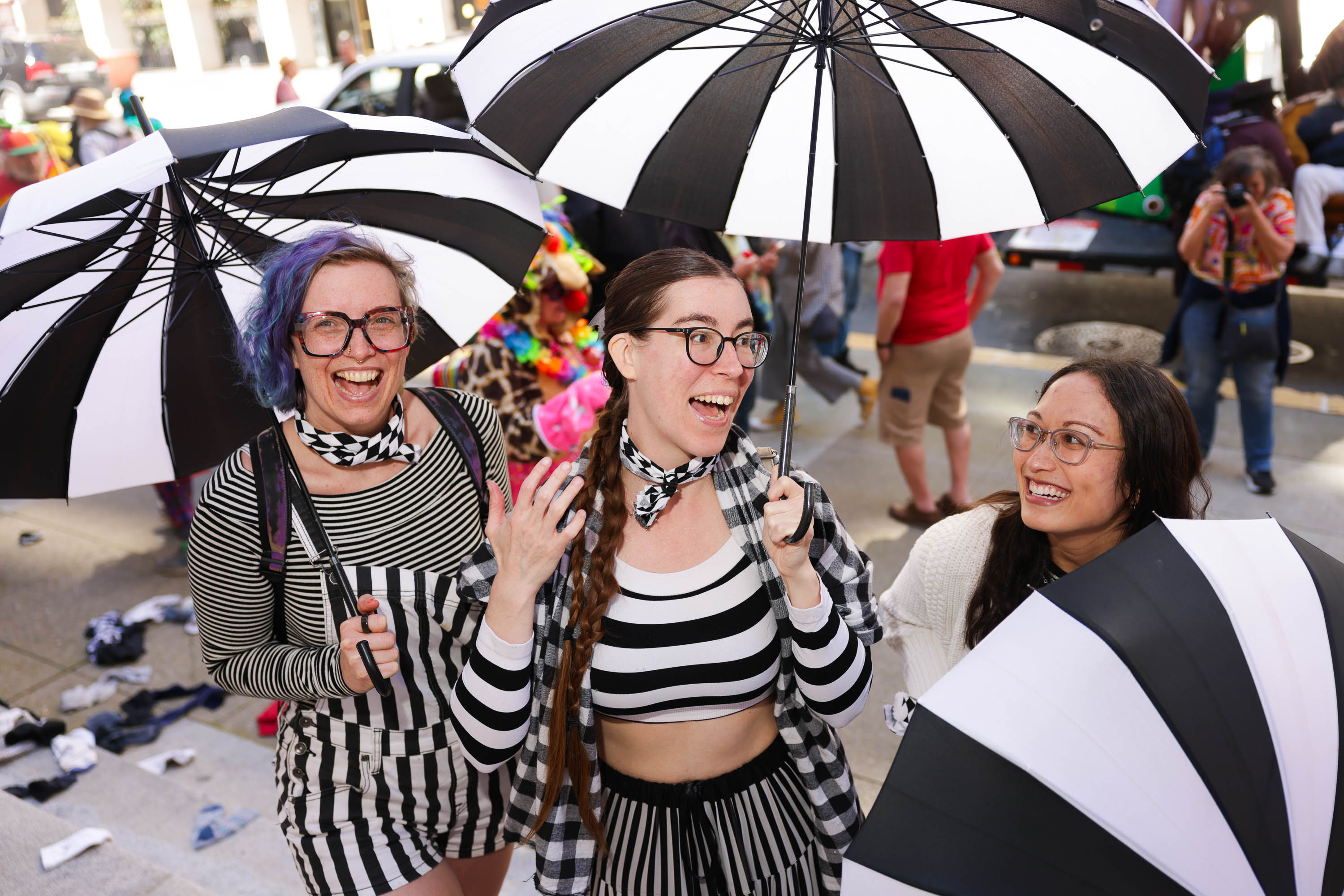 Three women are smiling under black and white striped umbrellas, wearing similar patterned clothing.