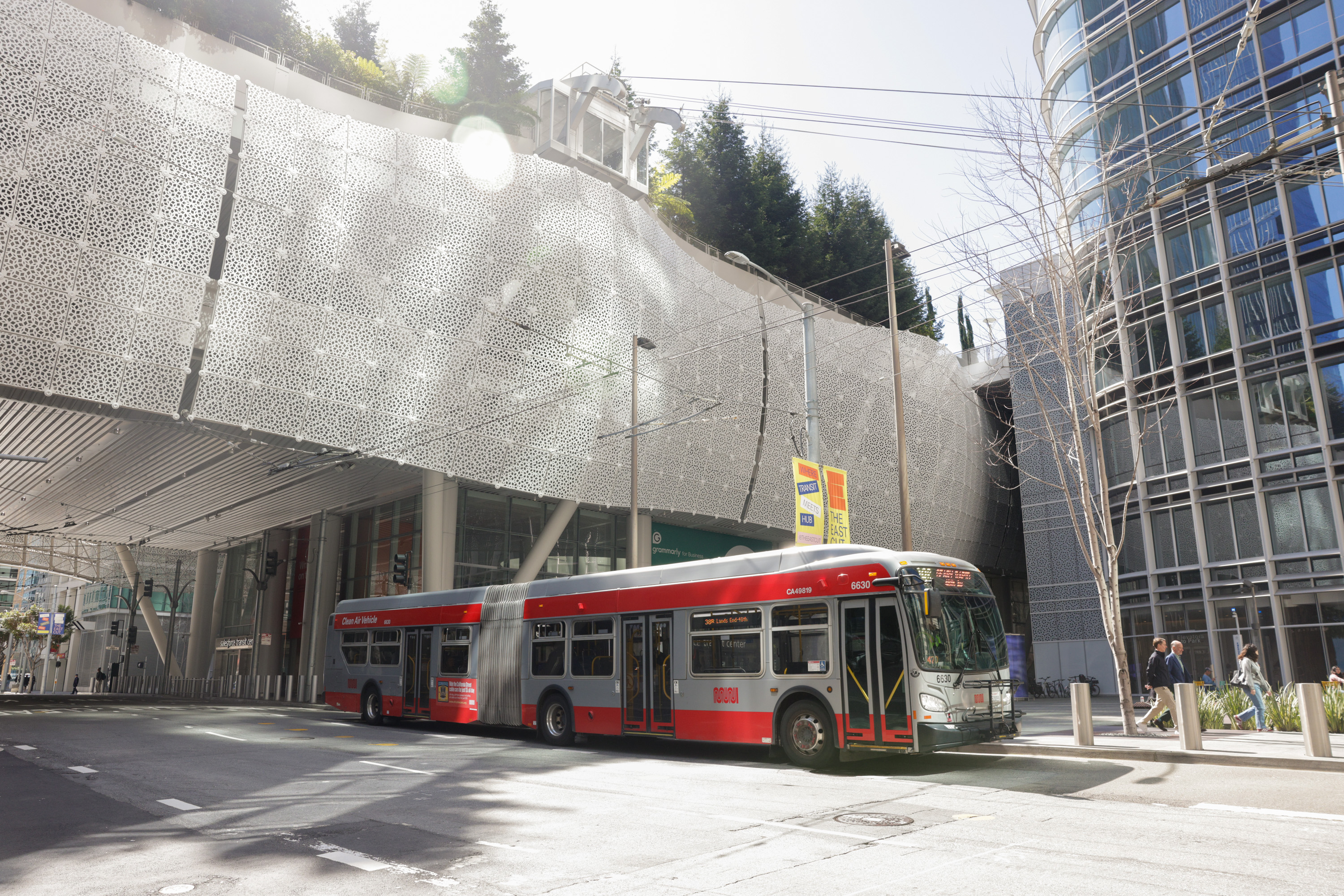 A red and silver city bus drives by the Salesforce Transit Center.