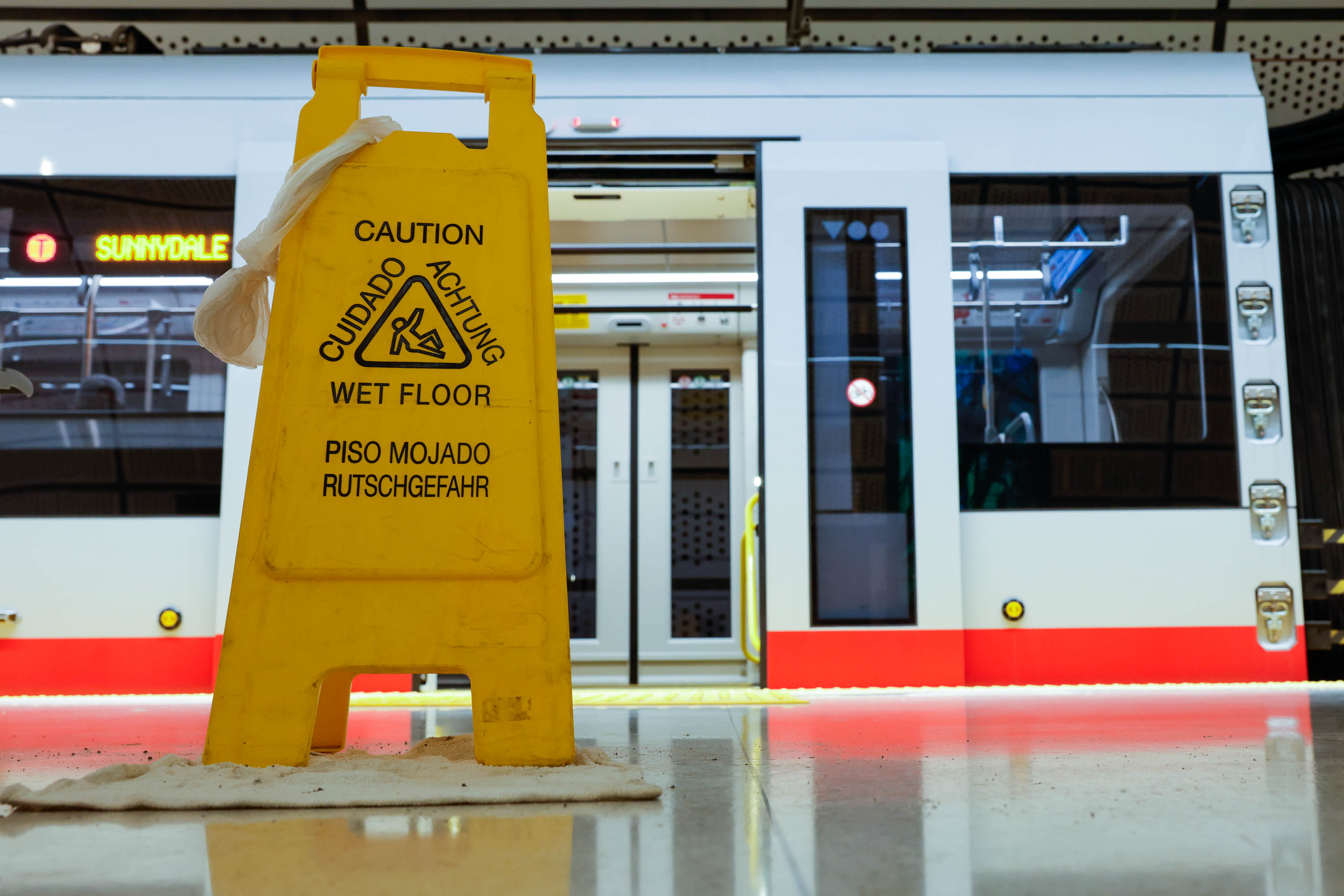 A &quot;Wet Floor&quot; sign in a train station foreground with a train in the background.