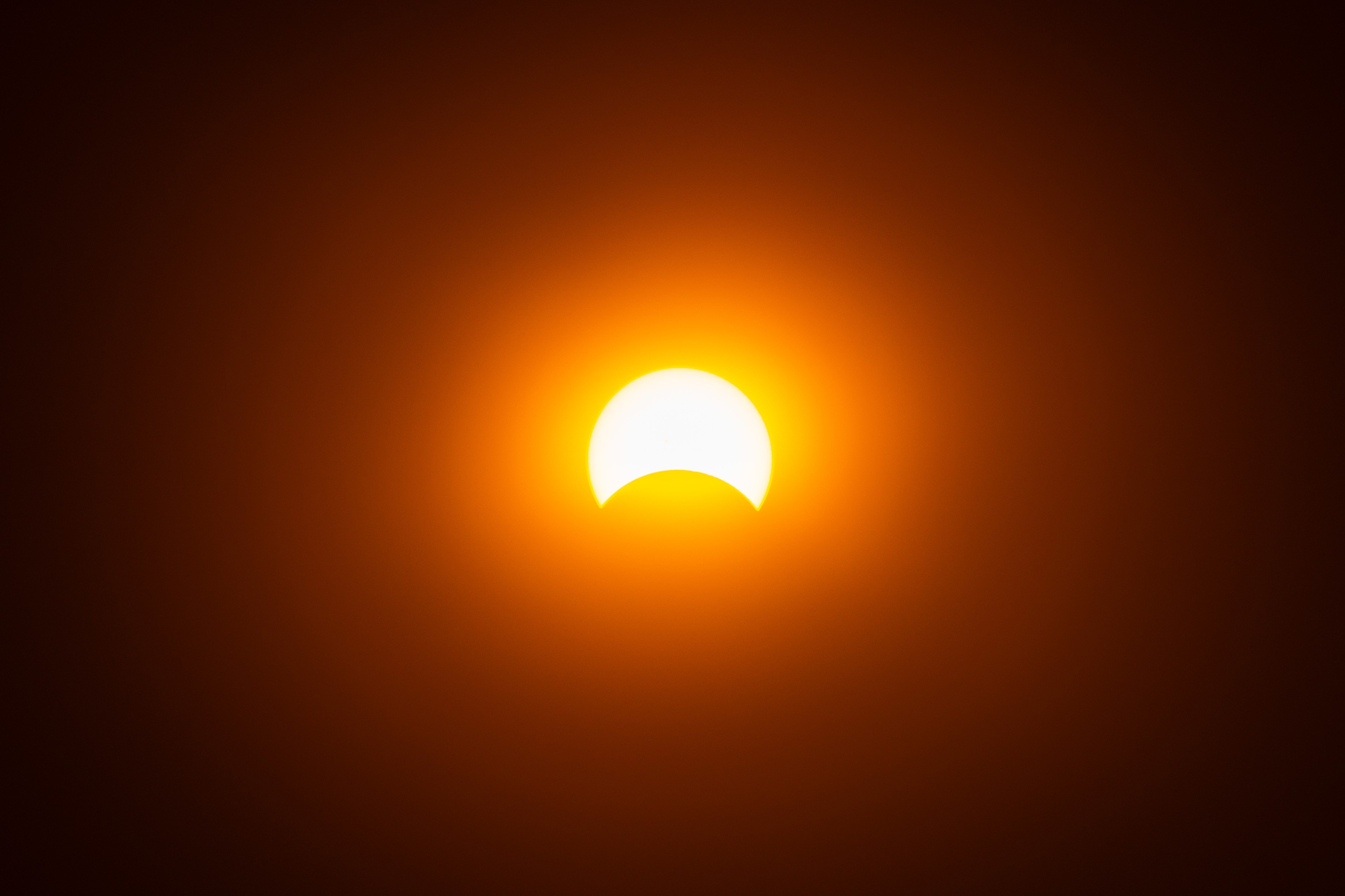 A solar eclipse; the Moon partially covers the Sun, against an orange sky.