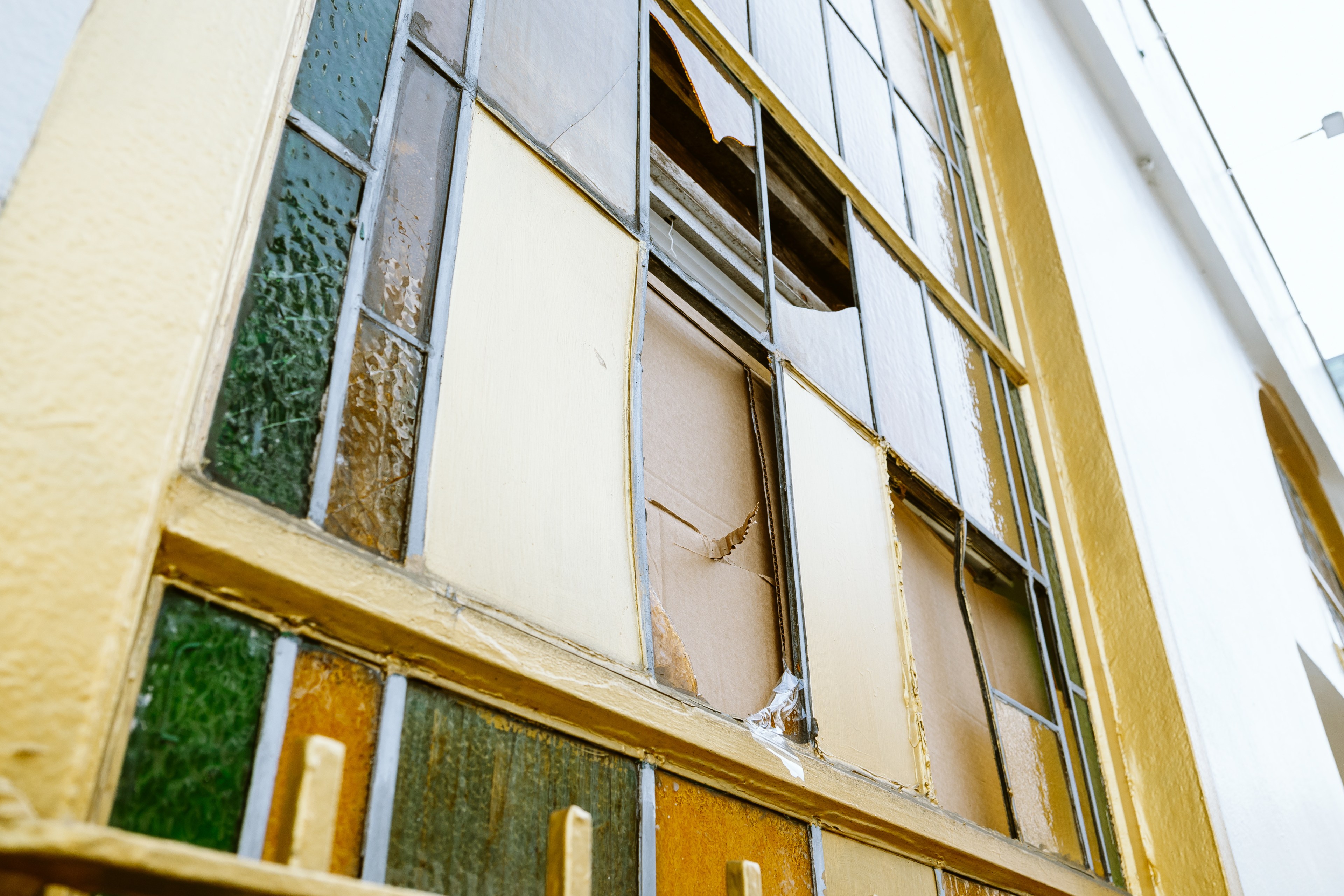 A broken stained-glass window with various colored panes, some shattered, in a yellow frame.