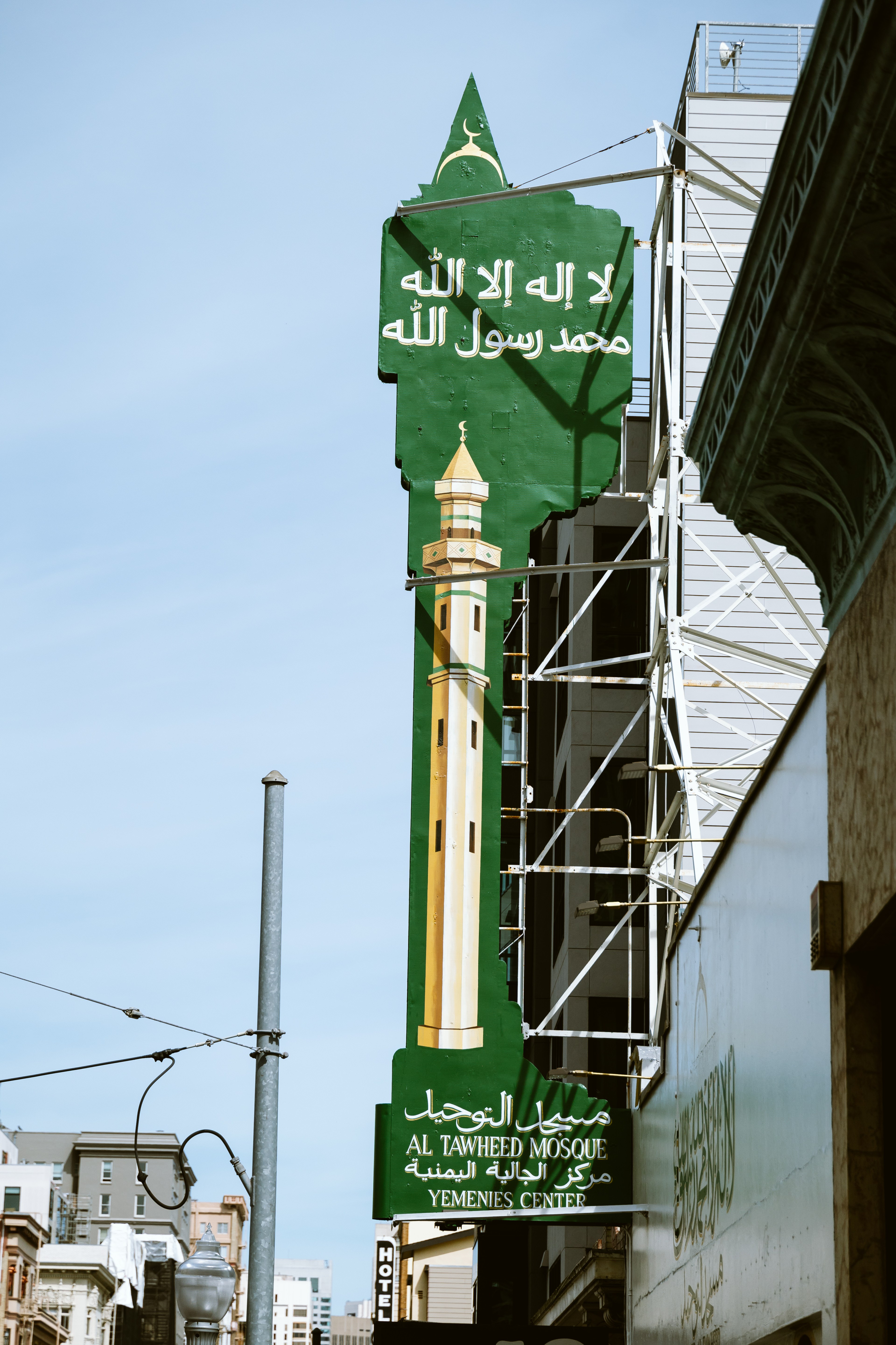 A green sign with Arabic text and &quot;AL TAWHEED MOSQUE&quot; written in English, on a building with a golden-domed minaret.