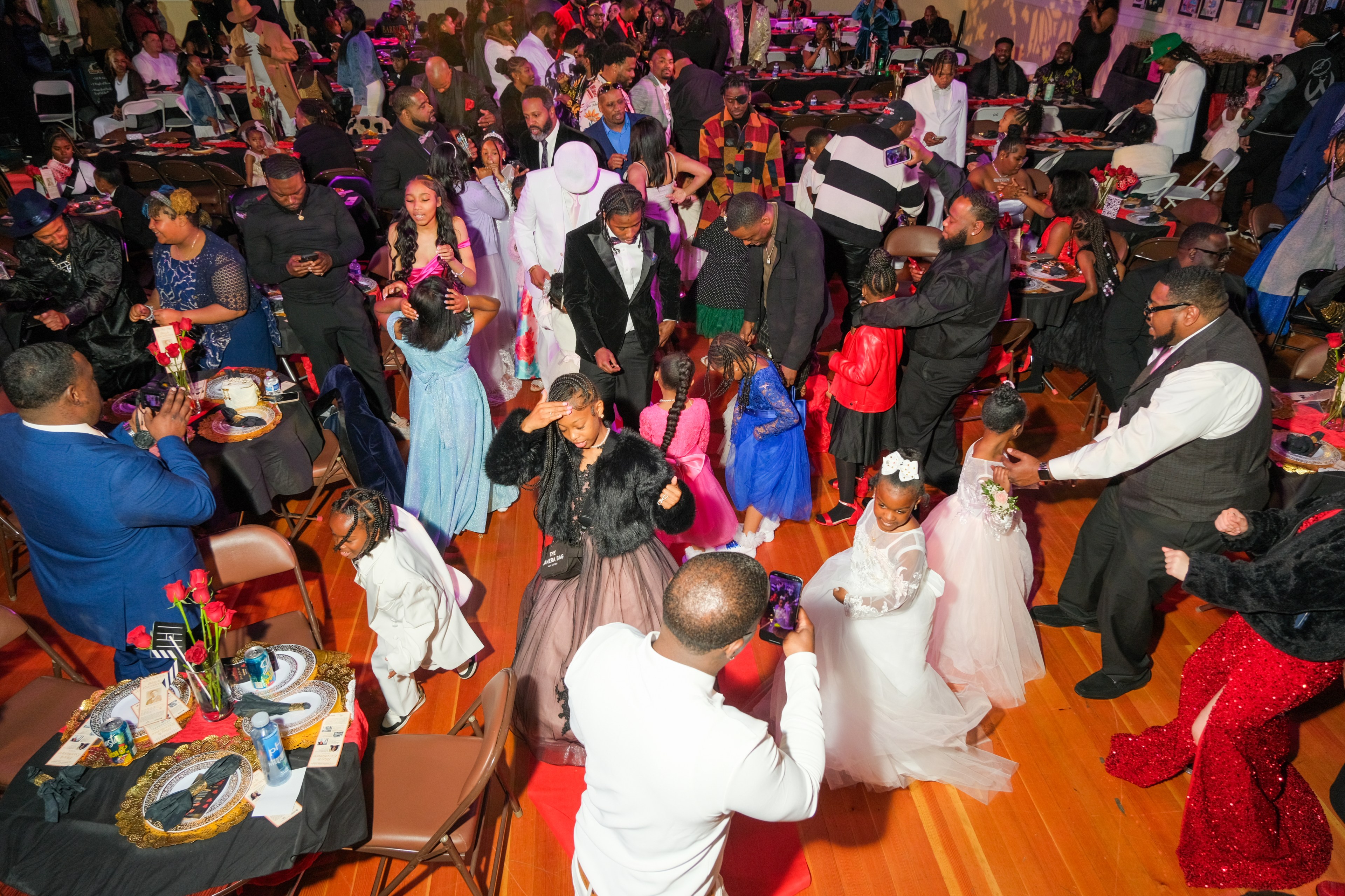 A lively indoor celebration with elegantly dressed adults and children mingling and dancing.