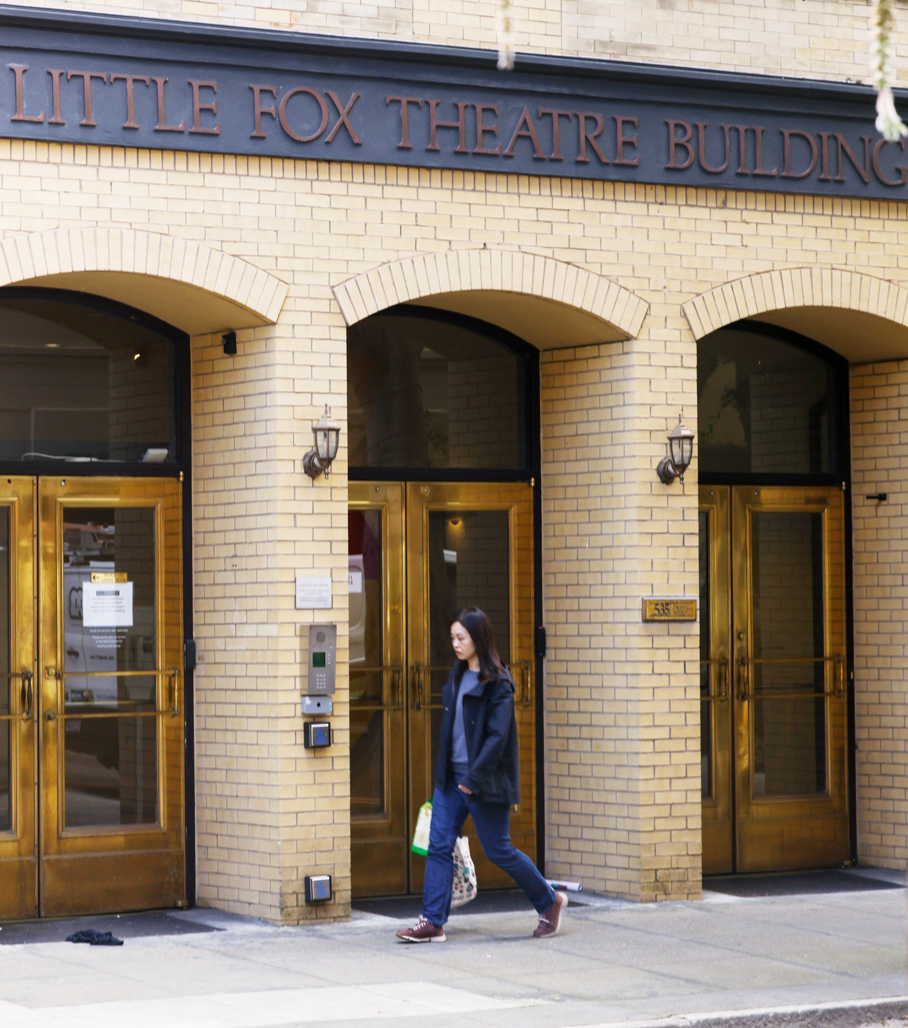 A person walks by the entrance of the &quot;Little Fox Theatre Building&quot; with arched doorways.