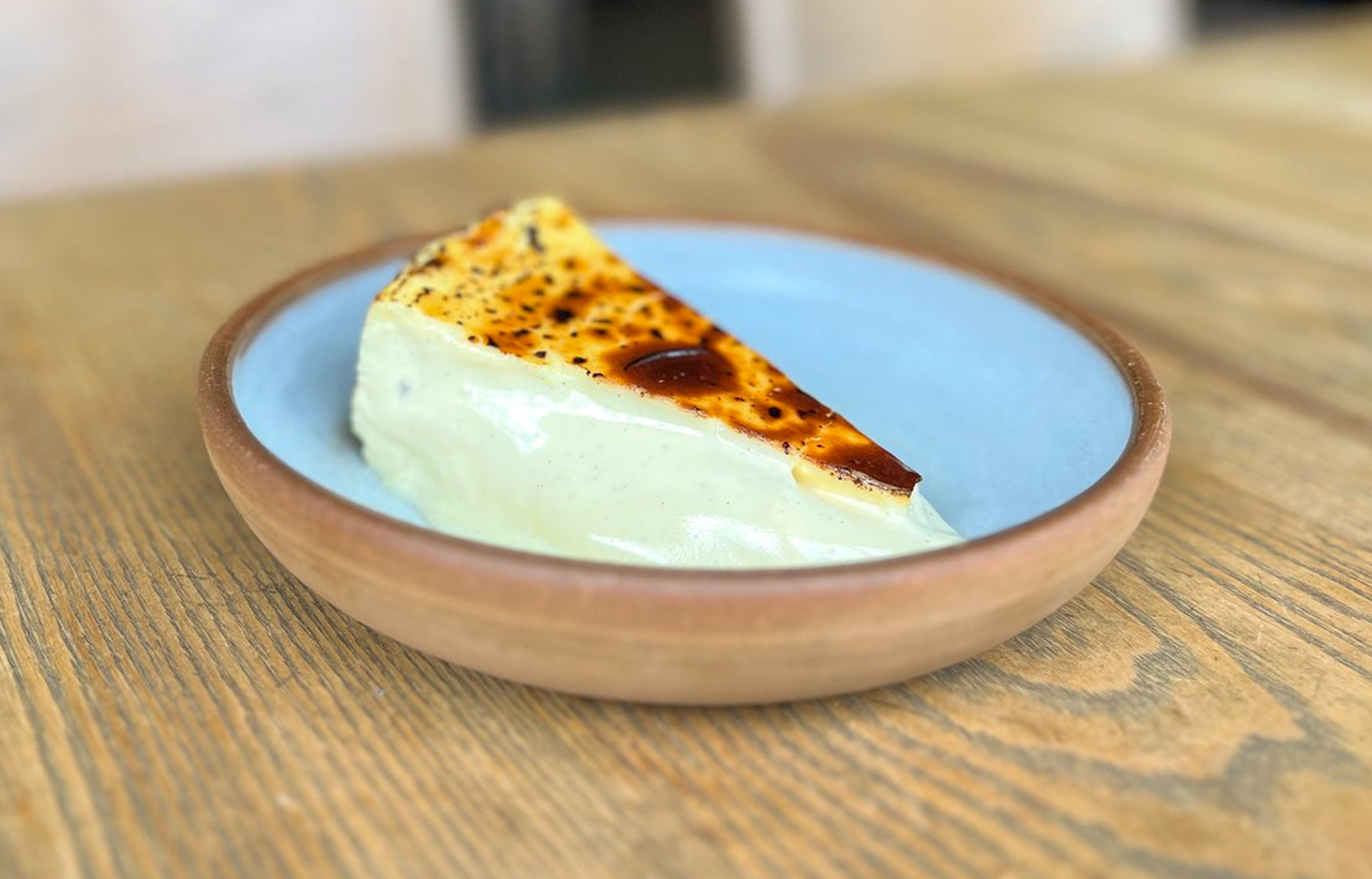 A slice of creamy cheesecake with a brûléed top on a blue plate.