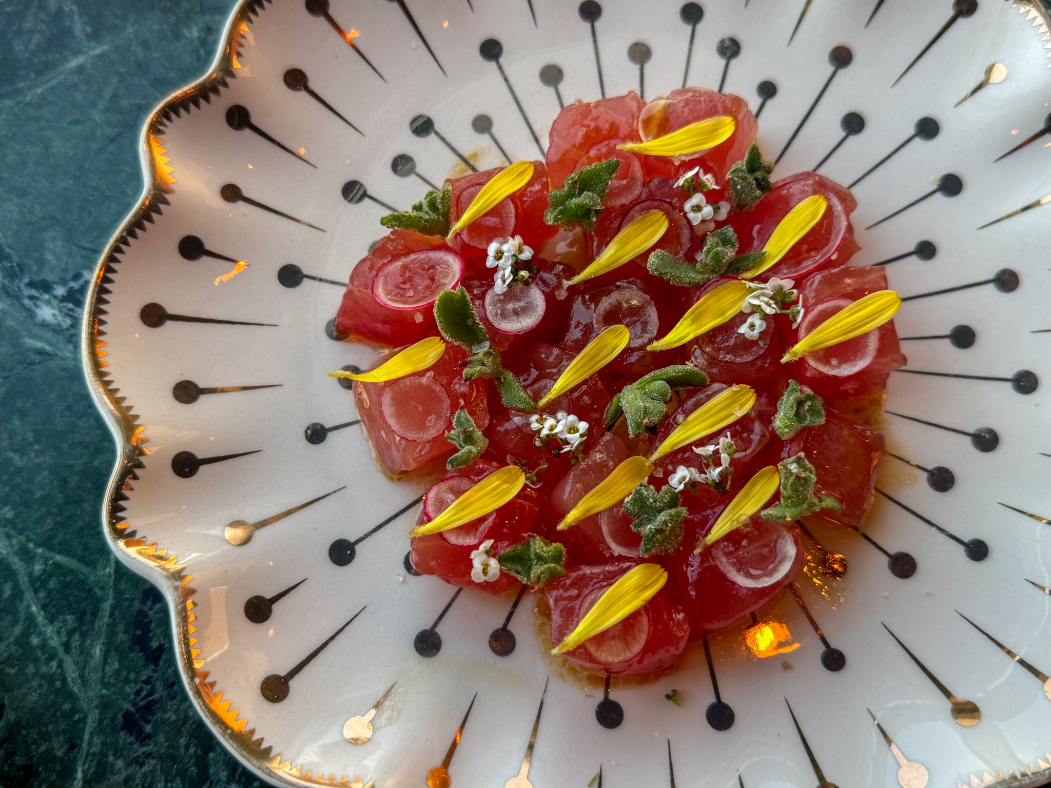 A plate of tuna tartare garnished with flower petals, herbs, and sauce dots.