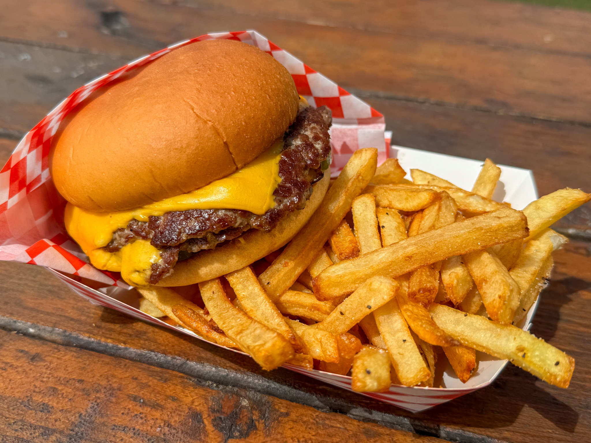A cheeseburger with fries in a checkered basket, on a wooden surface.