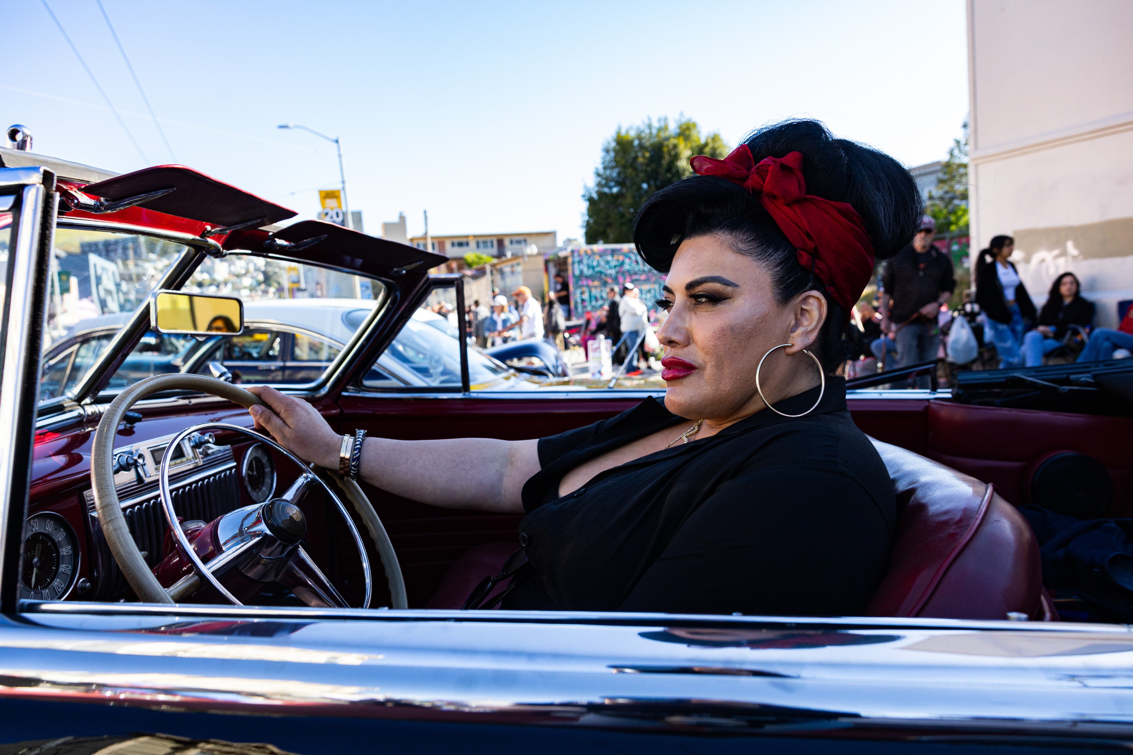 a woman in profile with an updo and red lips holds the steering wheel of a classic car