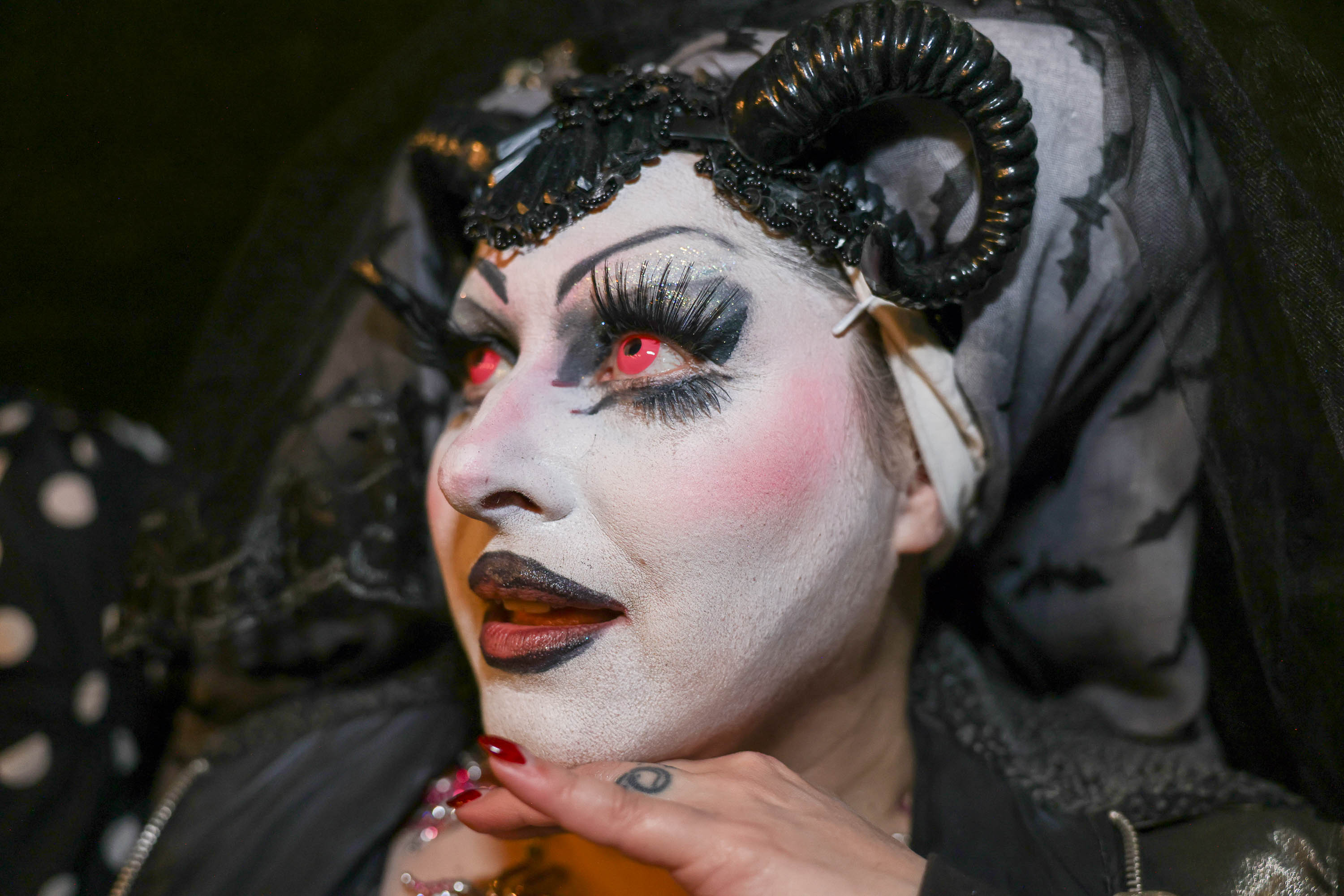 a closeup of a Sister of Perpetual Indulgence with black lips, red nails, white makeup and red contact lenses