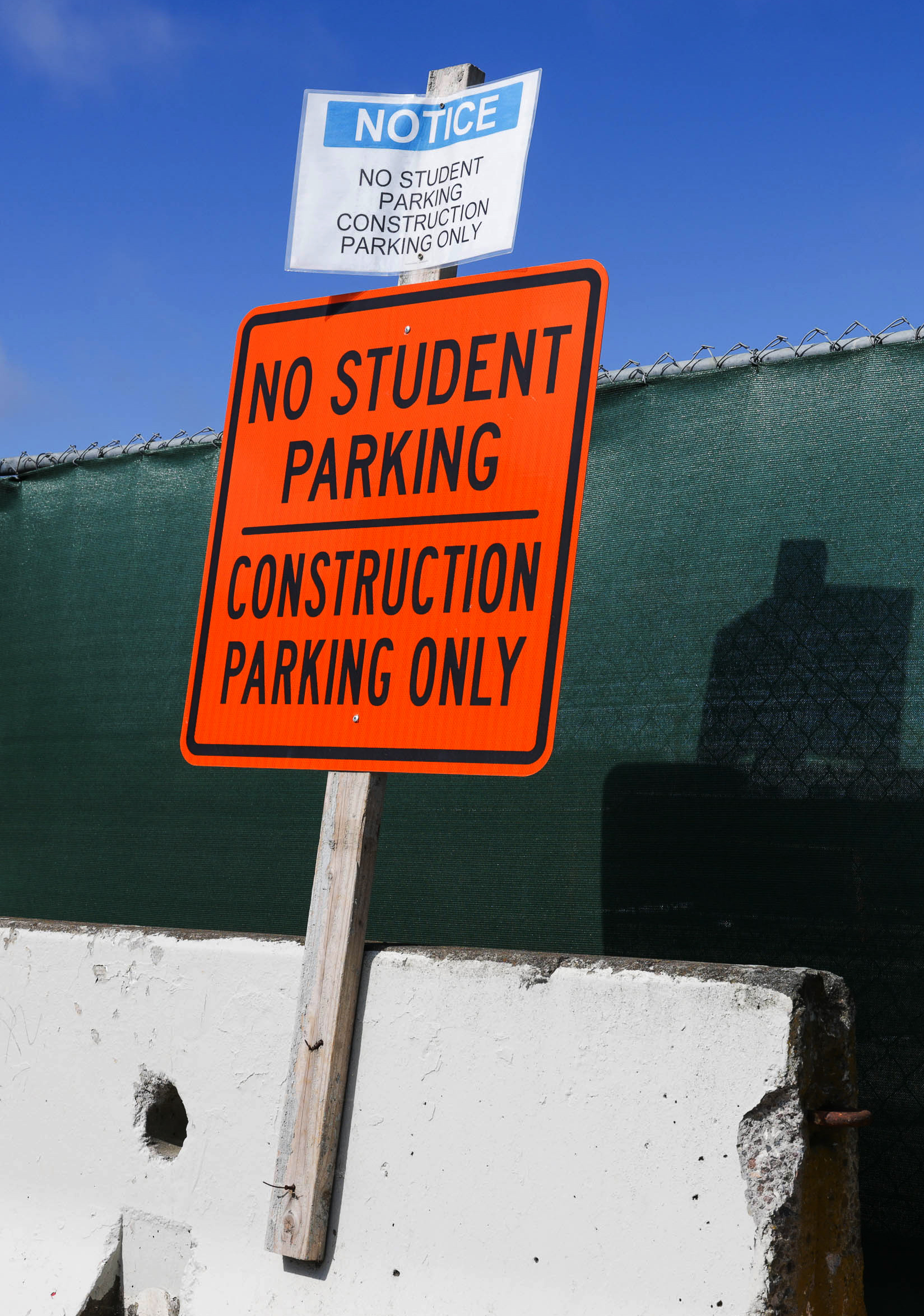Two signs on a post read &quot;NO STUDENT PARKING, CONSTRUCTION PARKING ONLY&quot;; one sign is orange, the other is white.