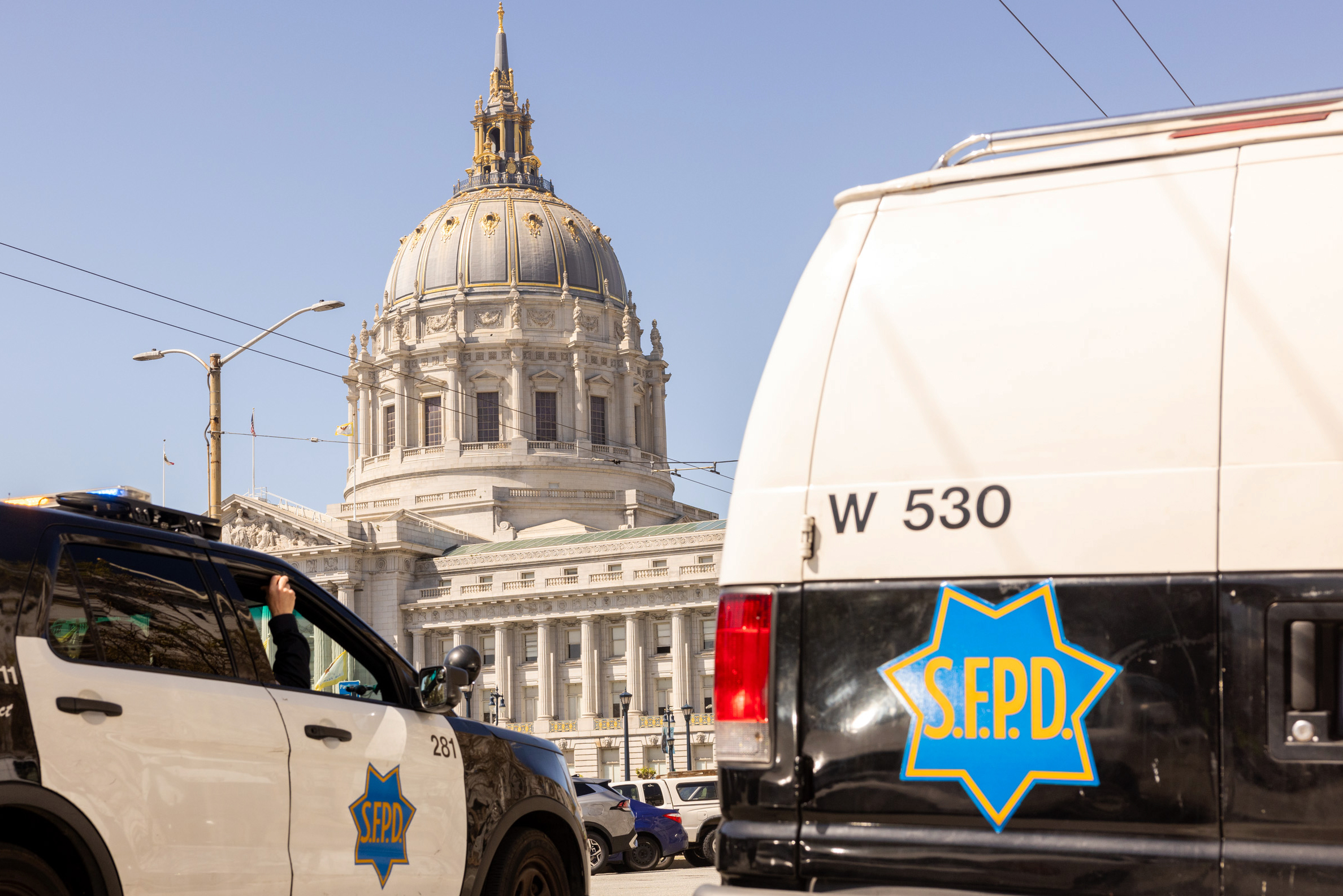 The image shows a grand domed building with intricate architecture in the background and two police vehicles labeled &quot;S.F.P.D.&quot; in the foreground.