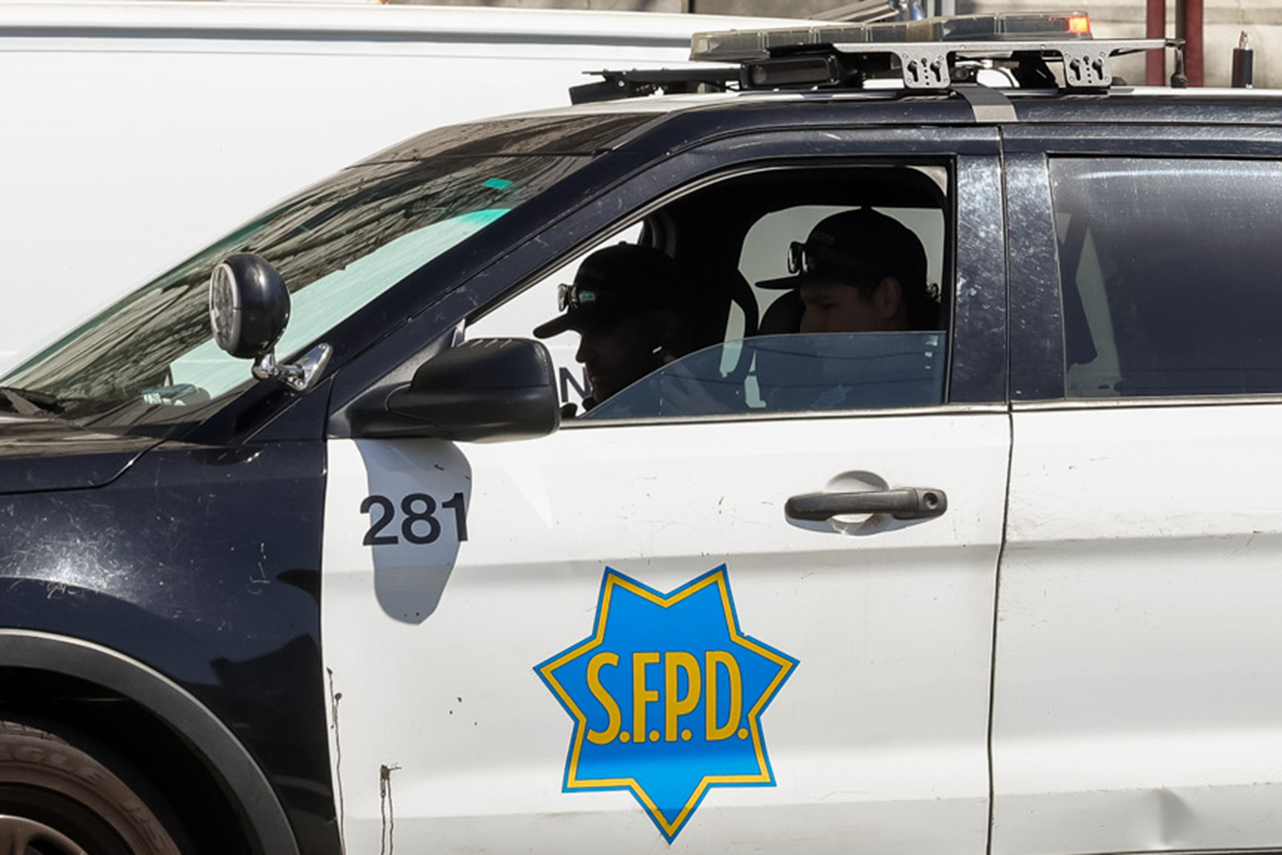 A police car with two officers inside; emblem reads &quot;S.F.P.D.&quot; on the door.