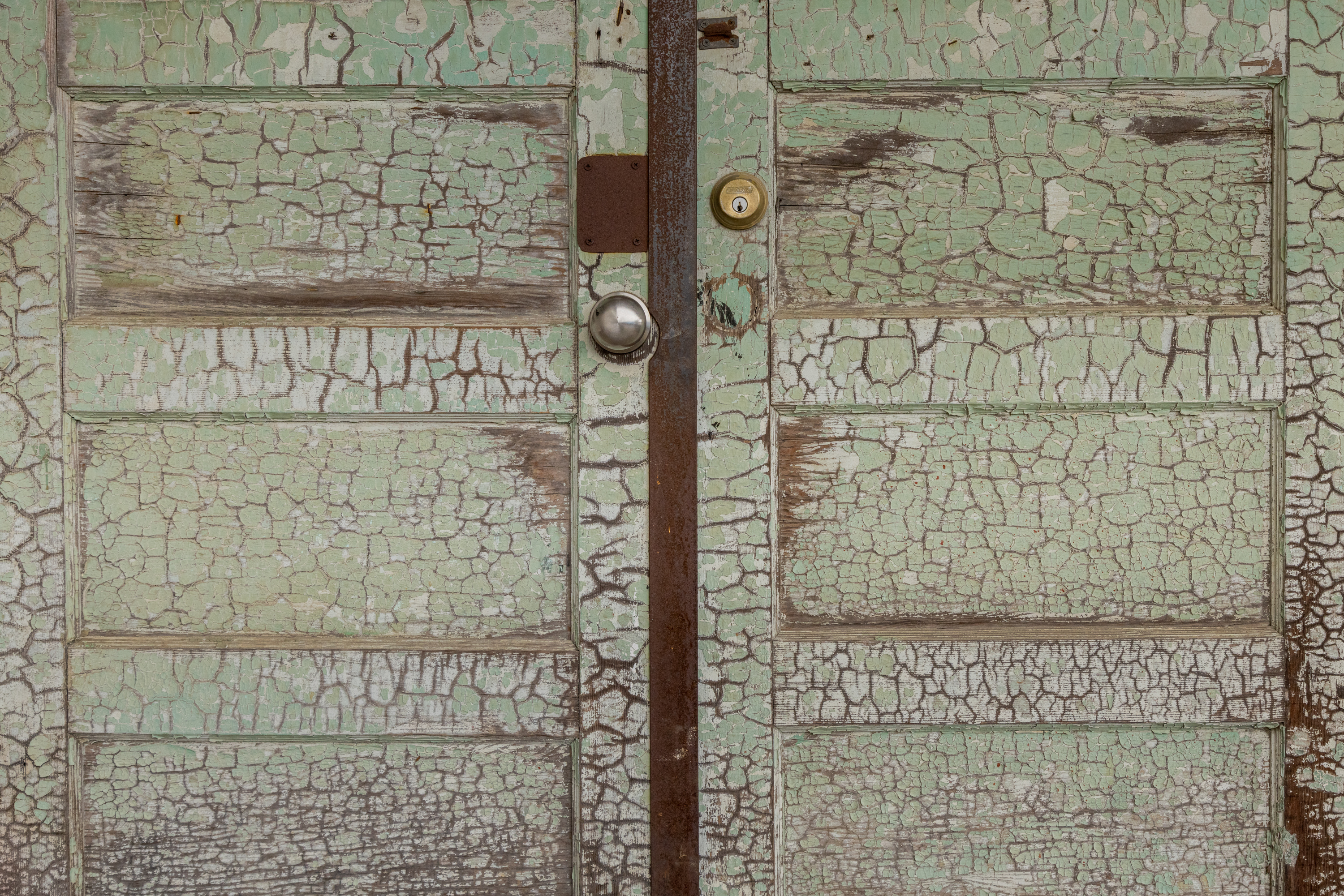 Aged green wooden door with cracked paint, metal knob, and keyhole.