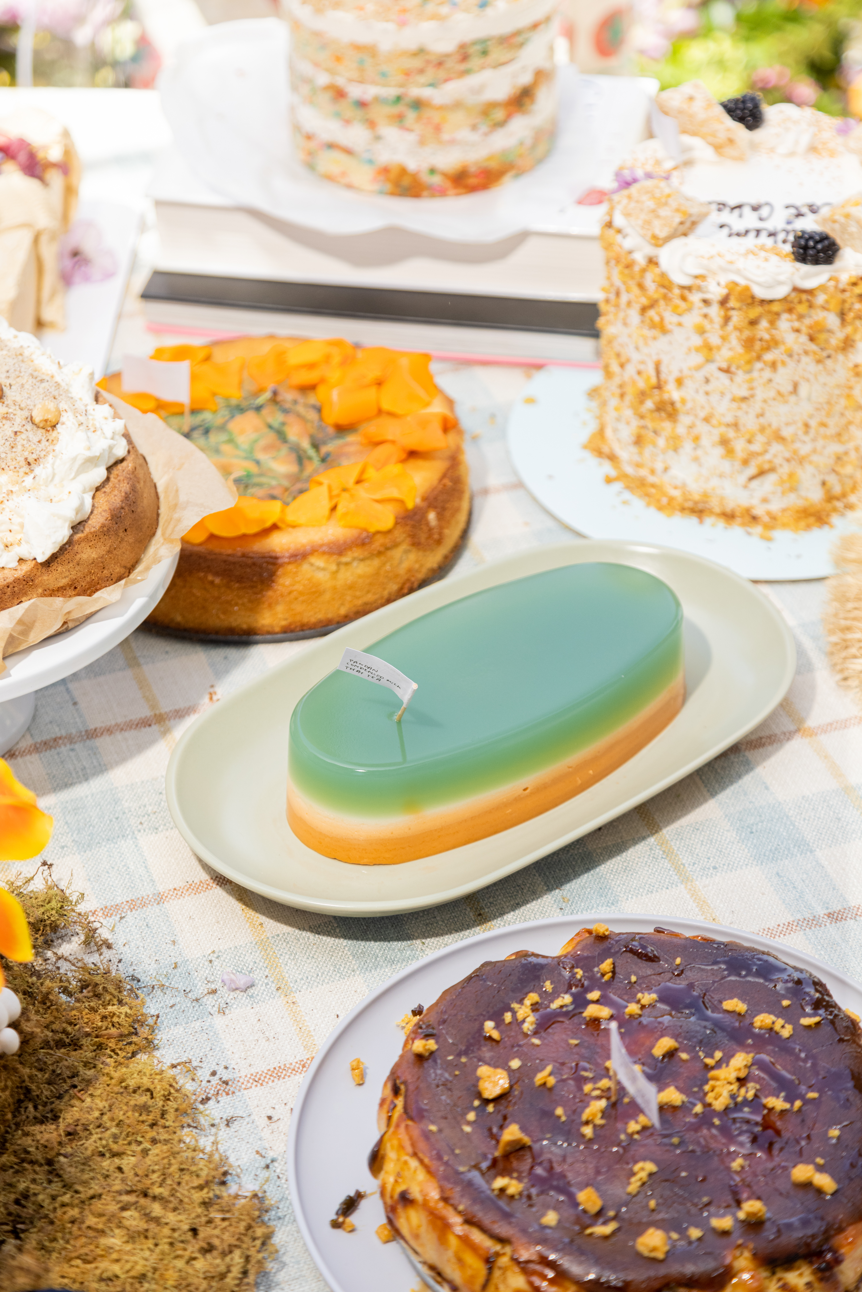 An assortment of colorful cakes on plates, one with a smooth, teal-glazed top.