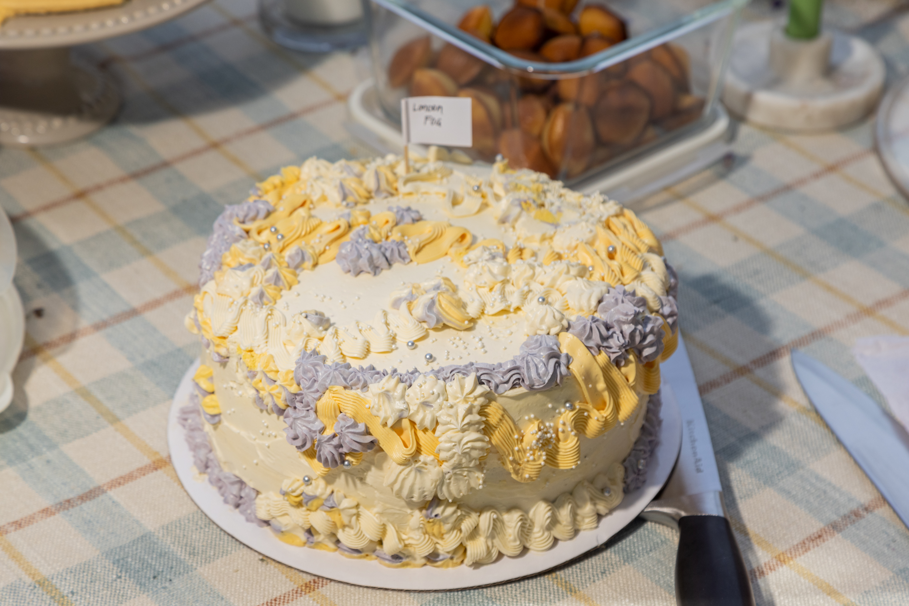 A cake with yellow and purple frosting on a checkered tablecloth next to a &quot;Lemon Fig&quot; sign.