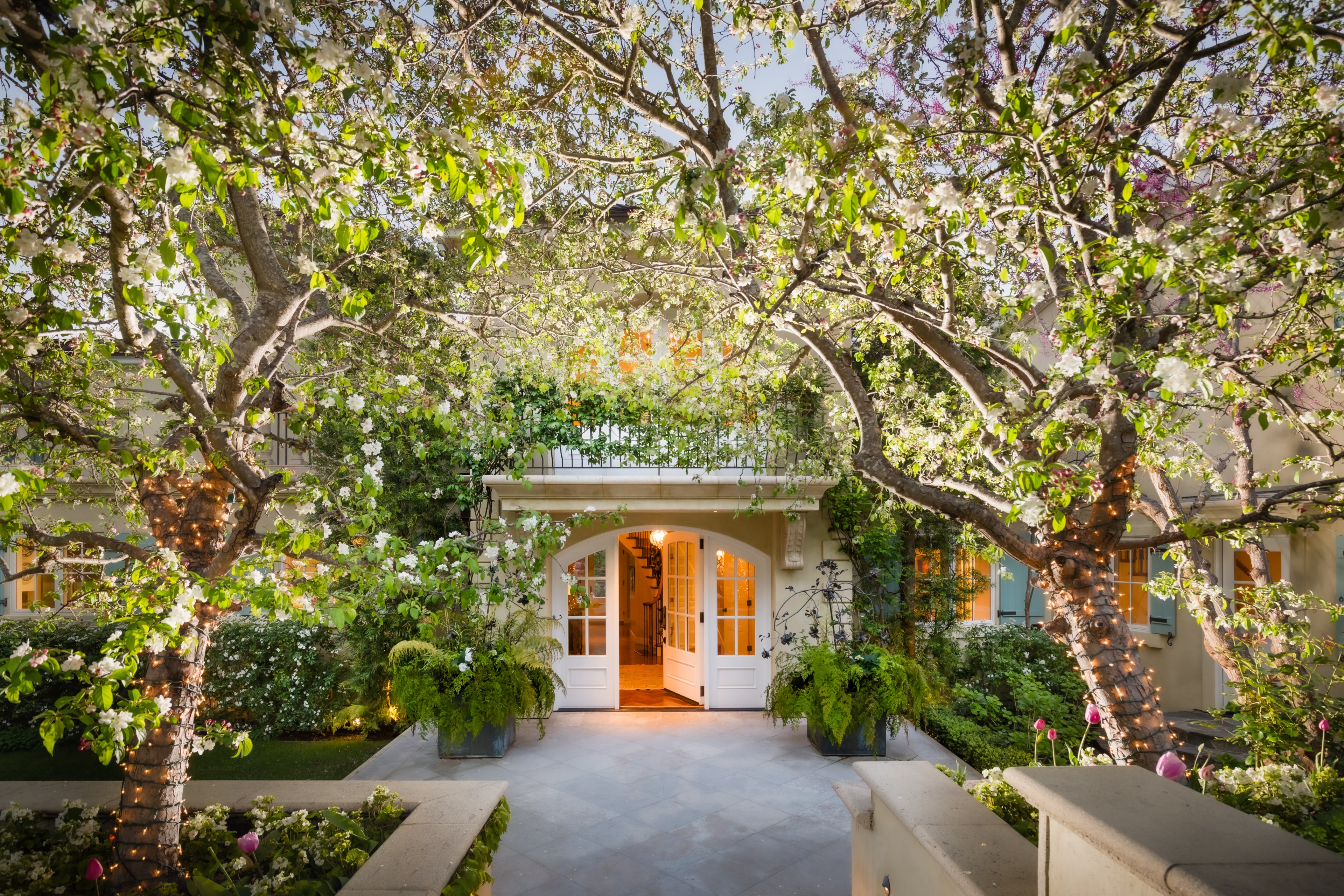 A serene house entrance flanked by blooming trees with a welcoming double door.