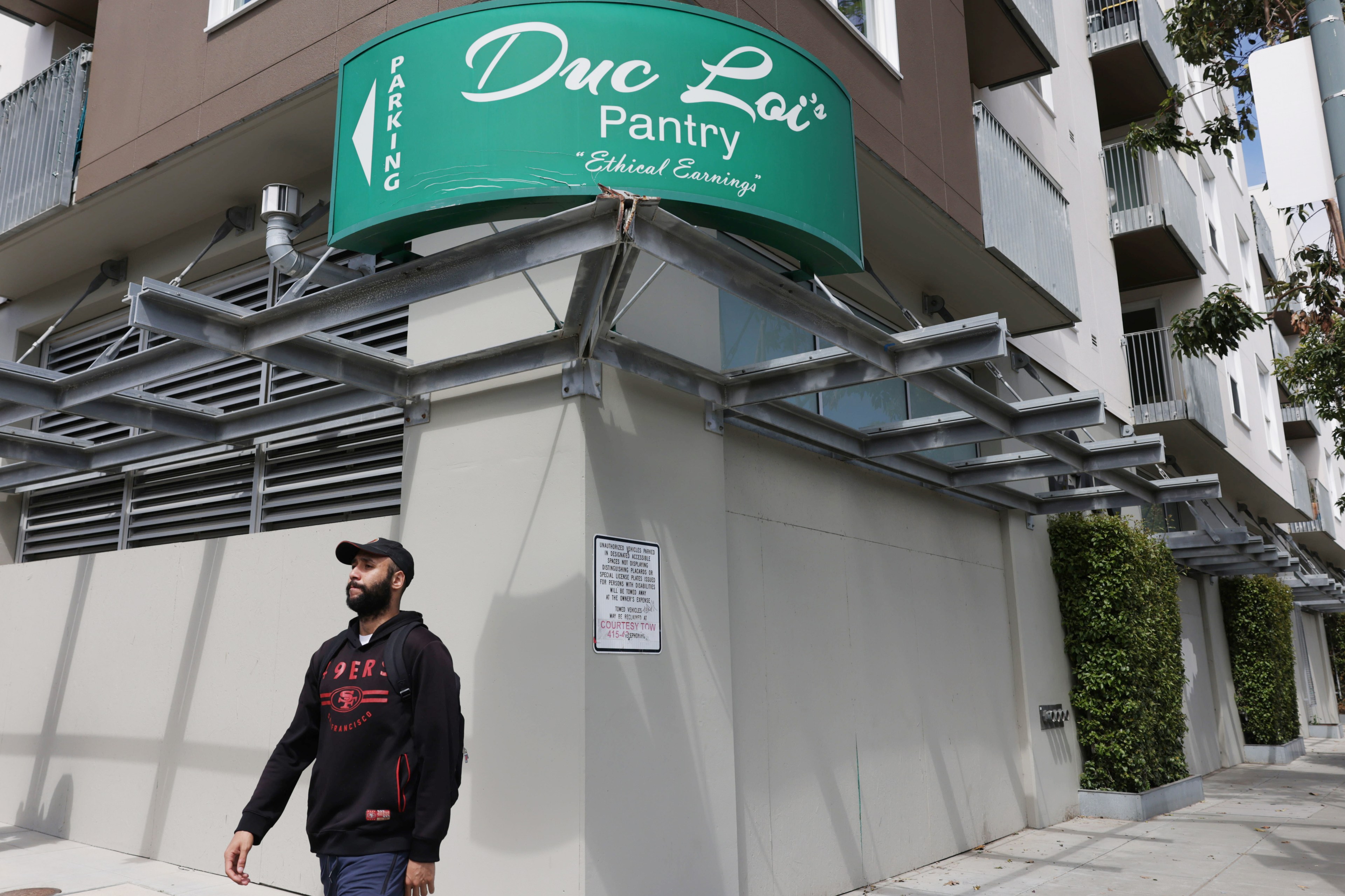 A man walks past a multi-story building with a "Duc Loi's Pantry" parking sign overhead.