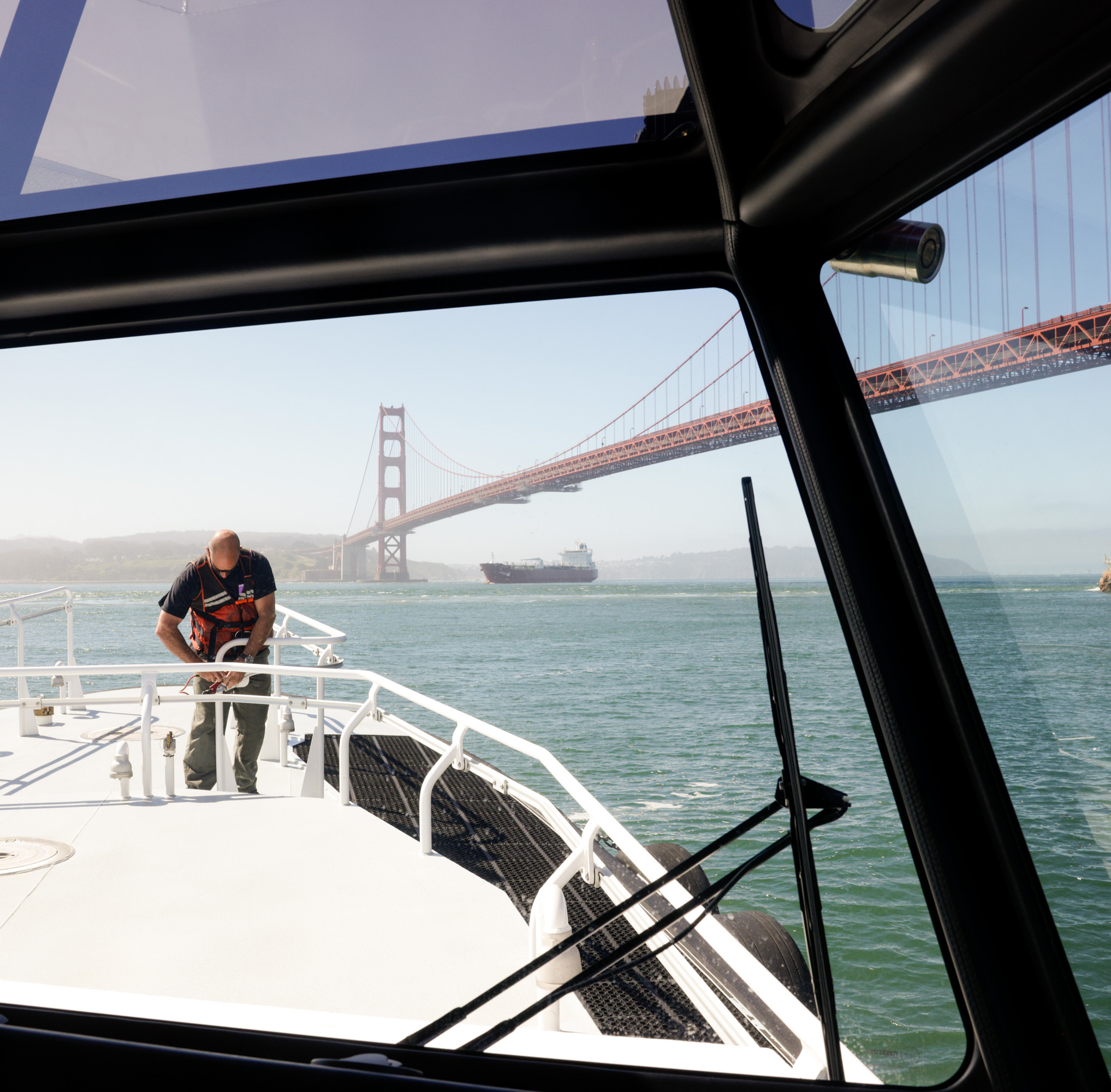 A man on a boat's bow with the Golden Gate Bridge and a ship in the background.