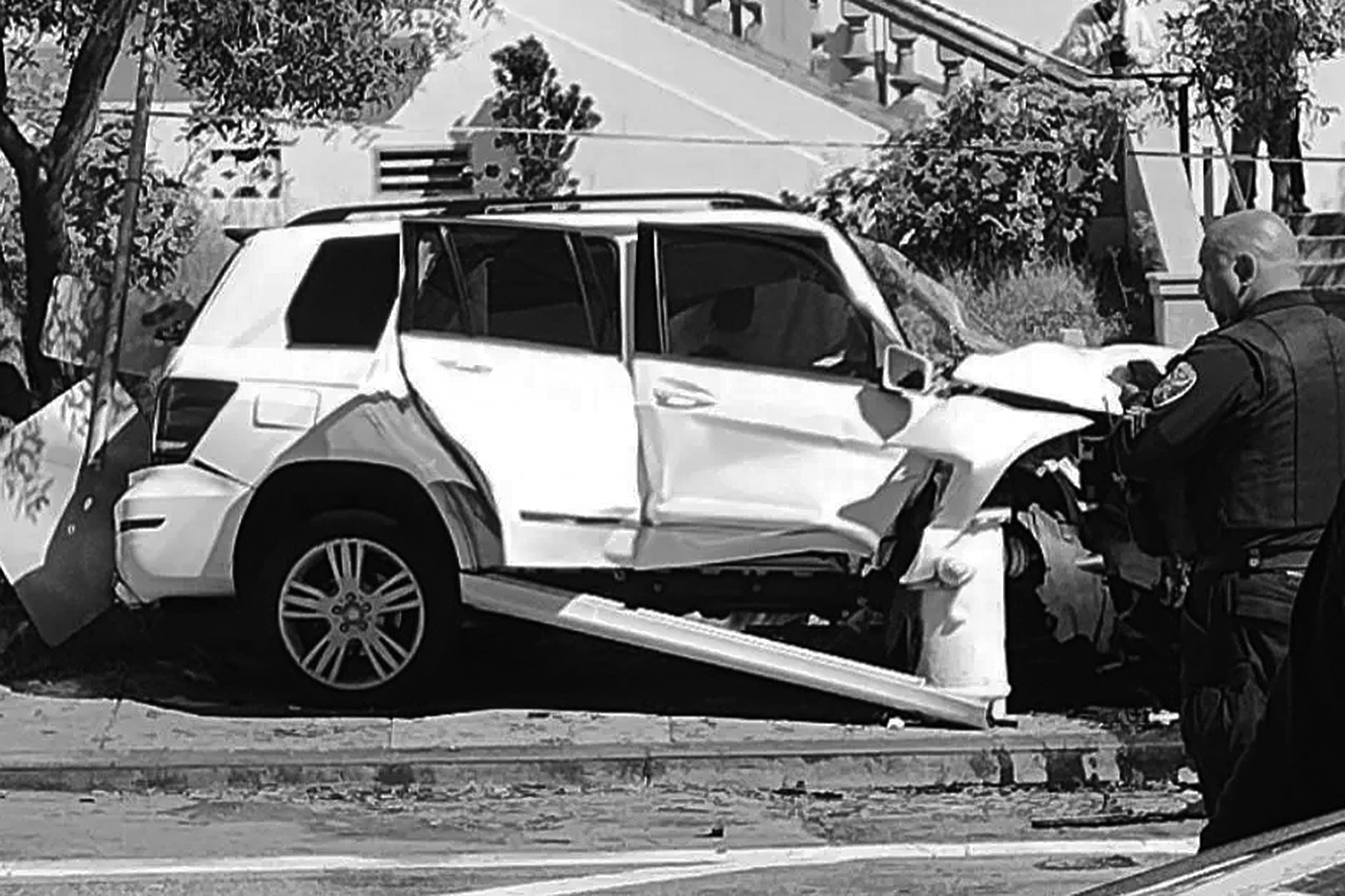 A policeman observes a severely damaged white SUV that crashed into a pole.