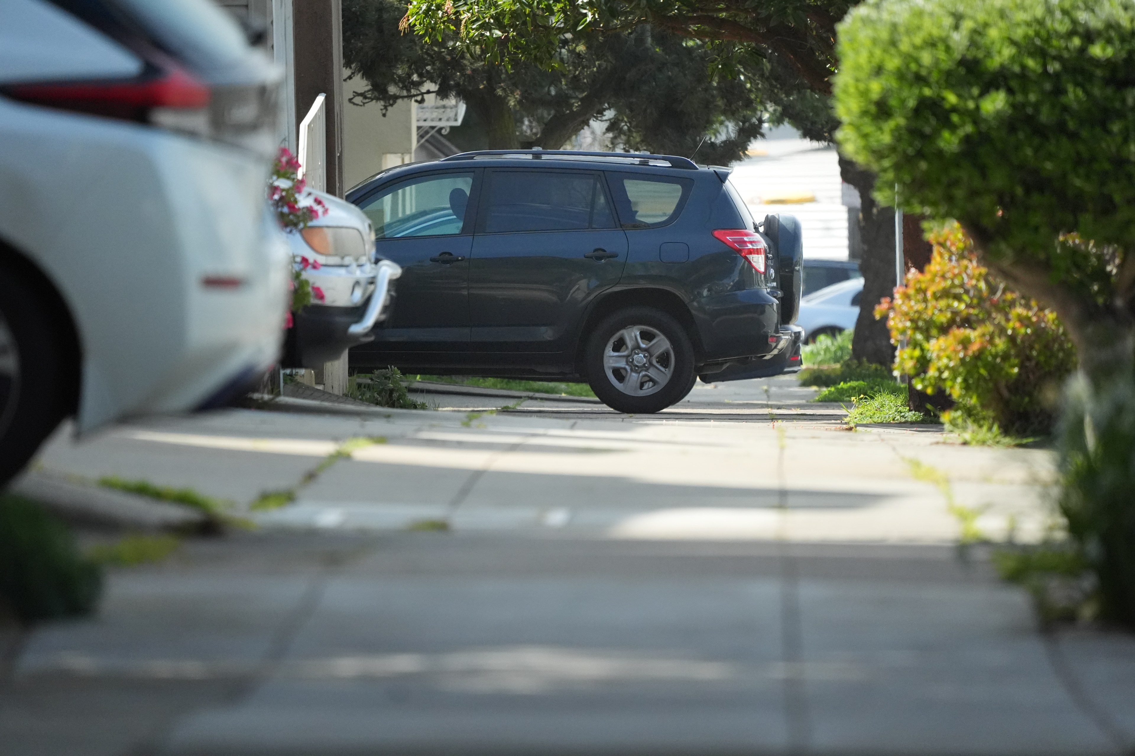 A car is parked on a sidewalk between houses, partially blocking the walkway.