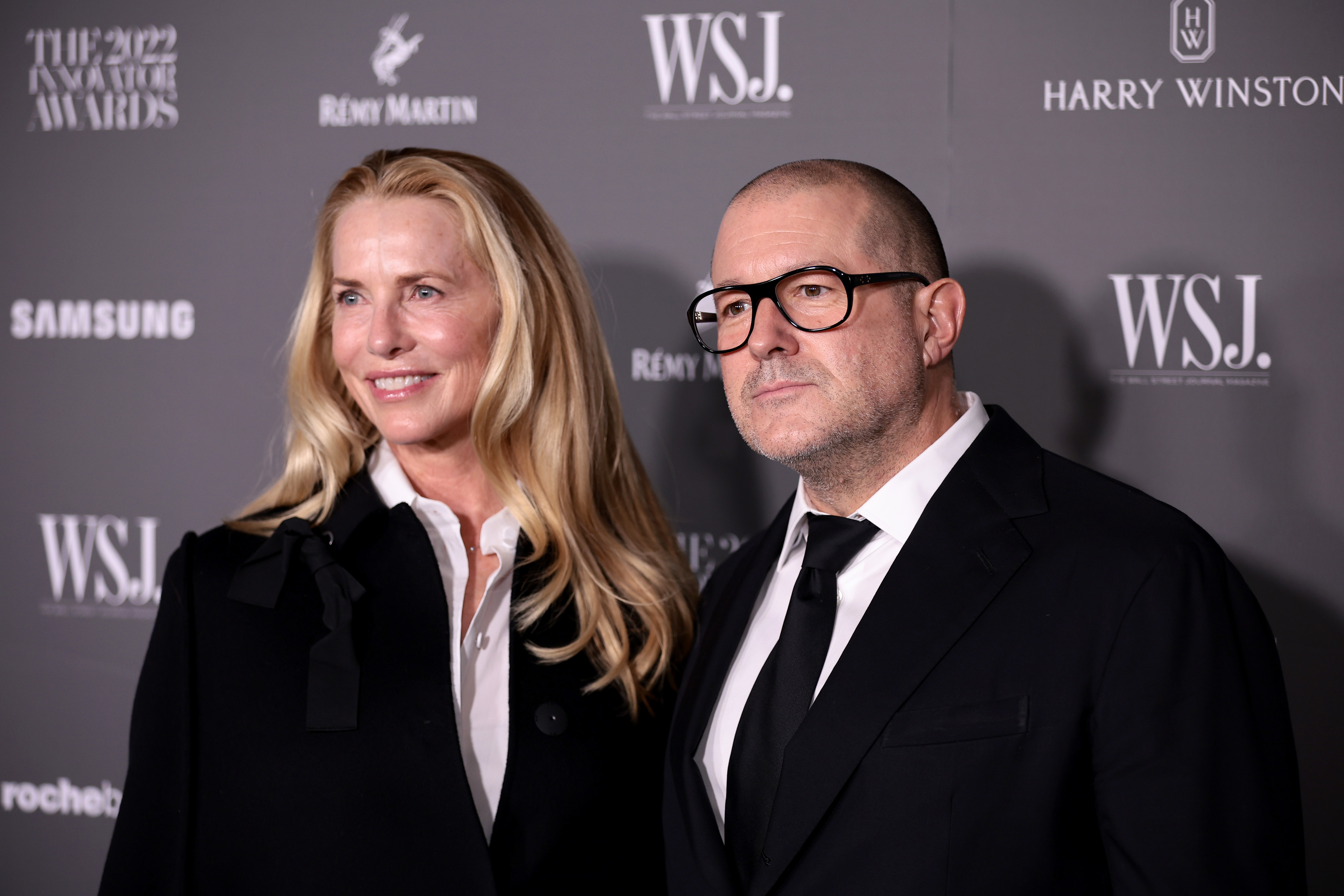 A man and woman in formal wear pose at a WSJ event, the woman slightly blurred.