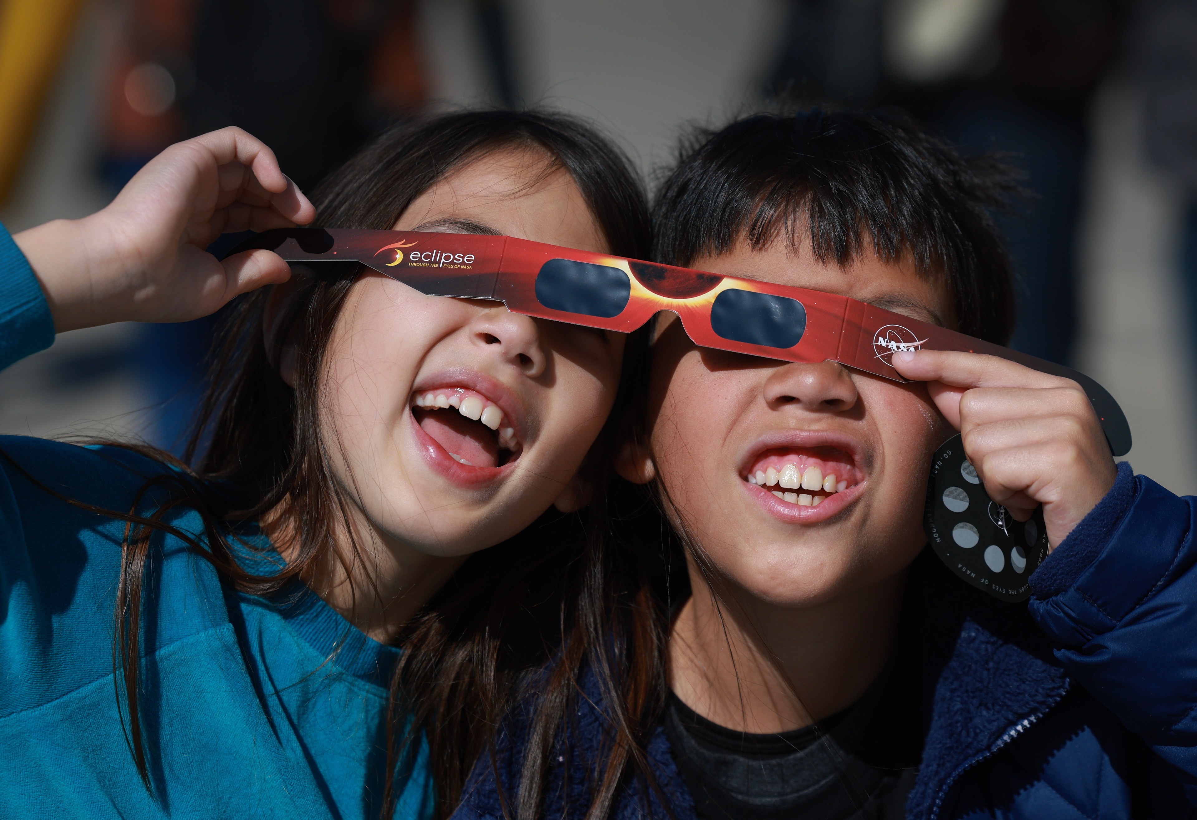 Two kids are smiling while sharing eclipse glasses.