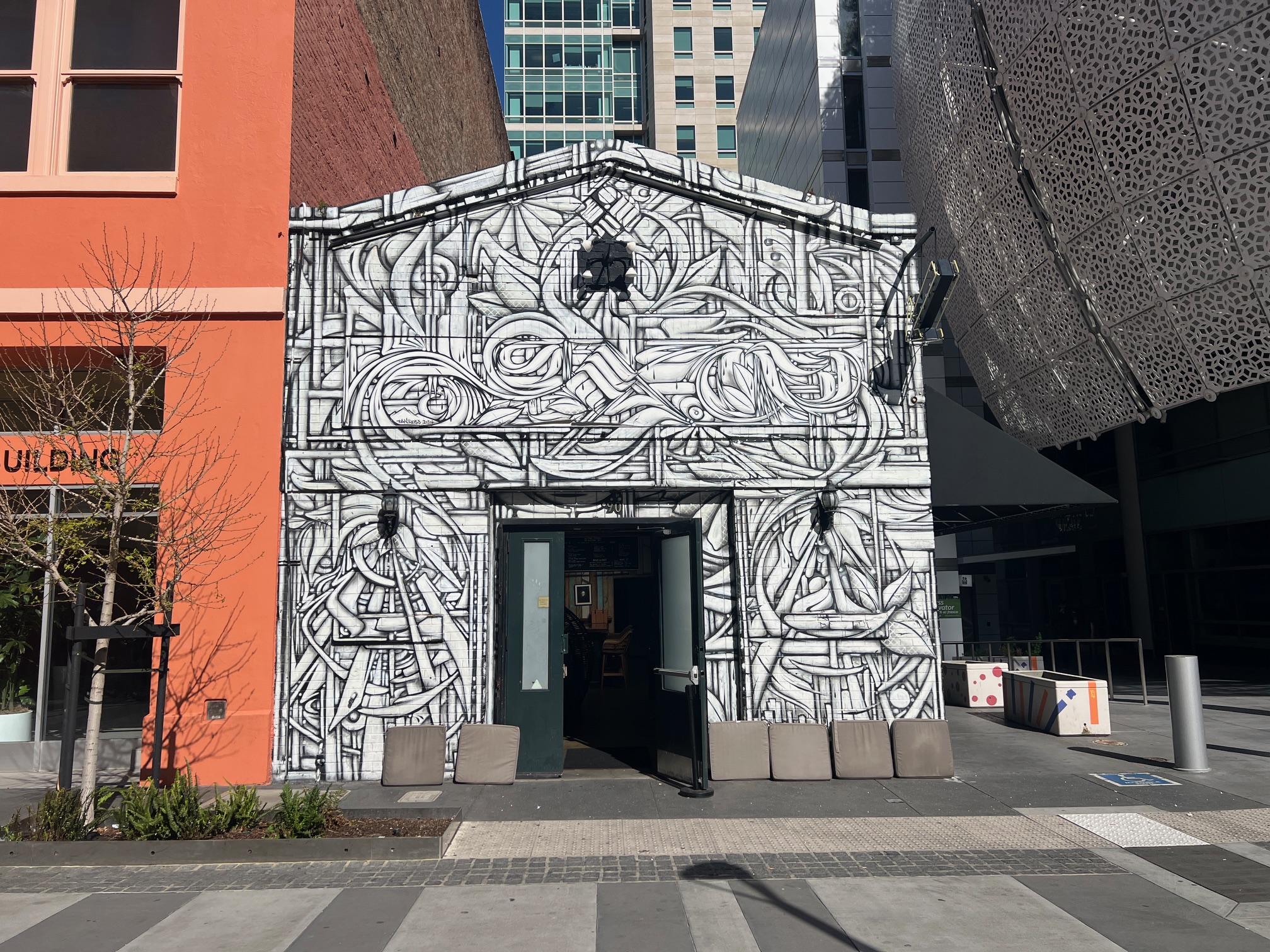 A building's facade is adorned with a large, intricate black and white mural with abstract figures and patterns.