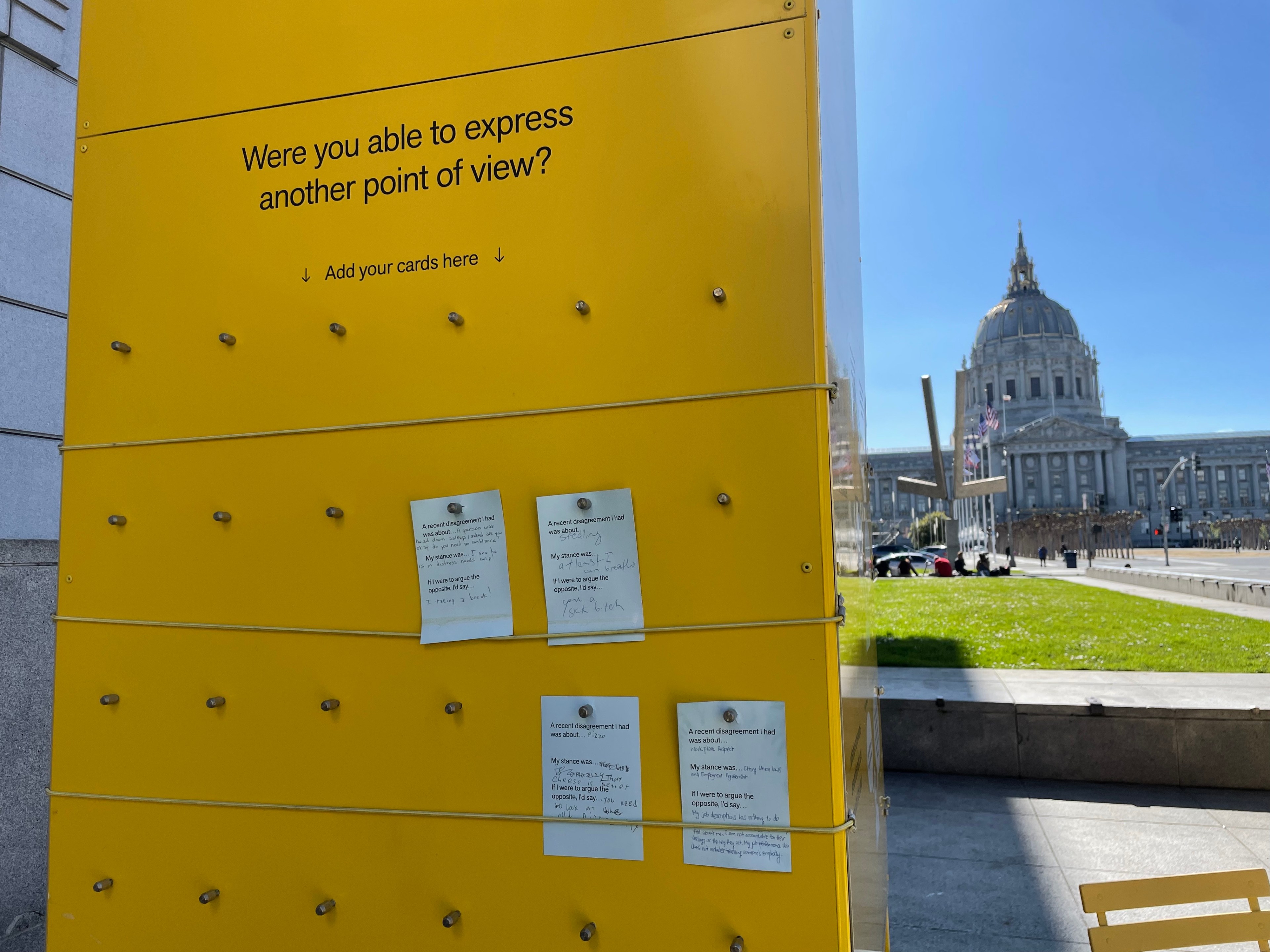 A yellow board with notes asking about expressing points of view, with a grand building and a clear sky in the background.