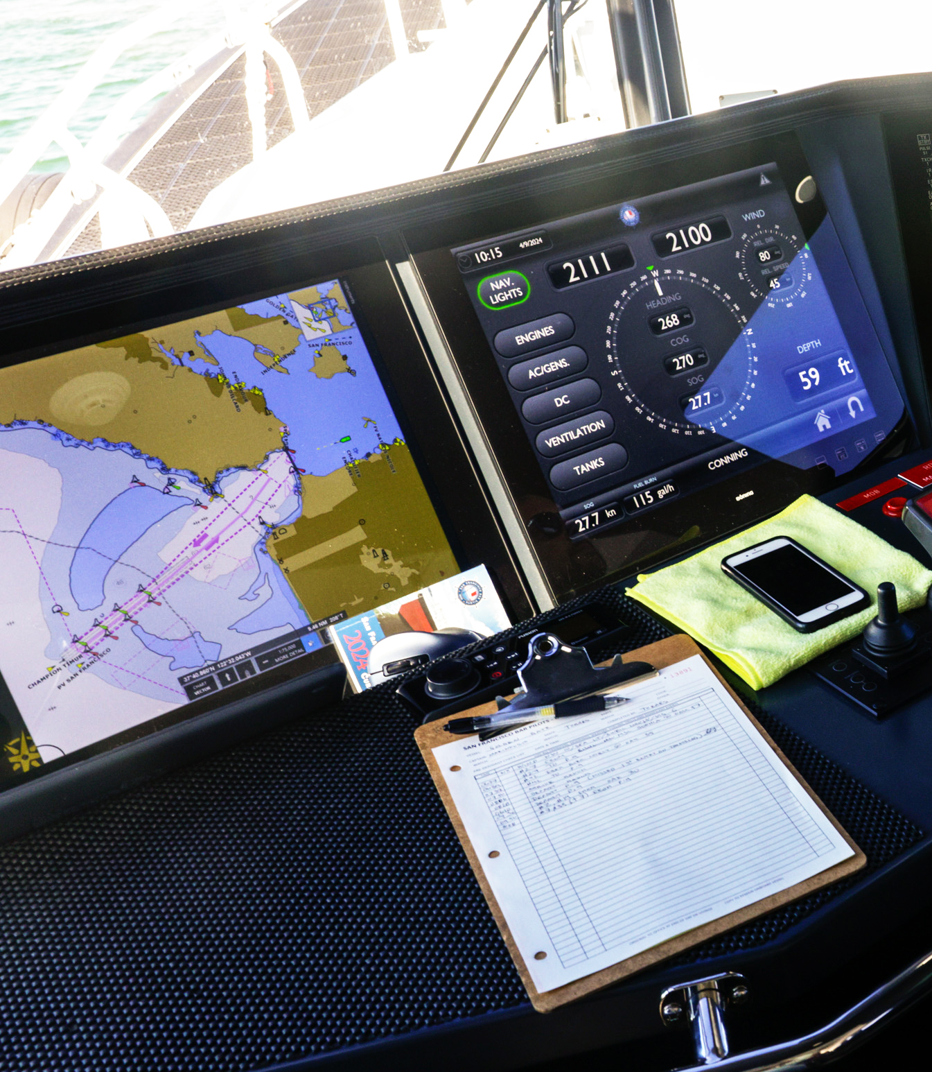 Boat navigation screens, a clipboard, and controls on a dashboard, with the ocean visible through a window.
