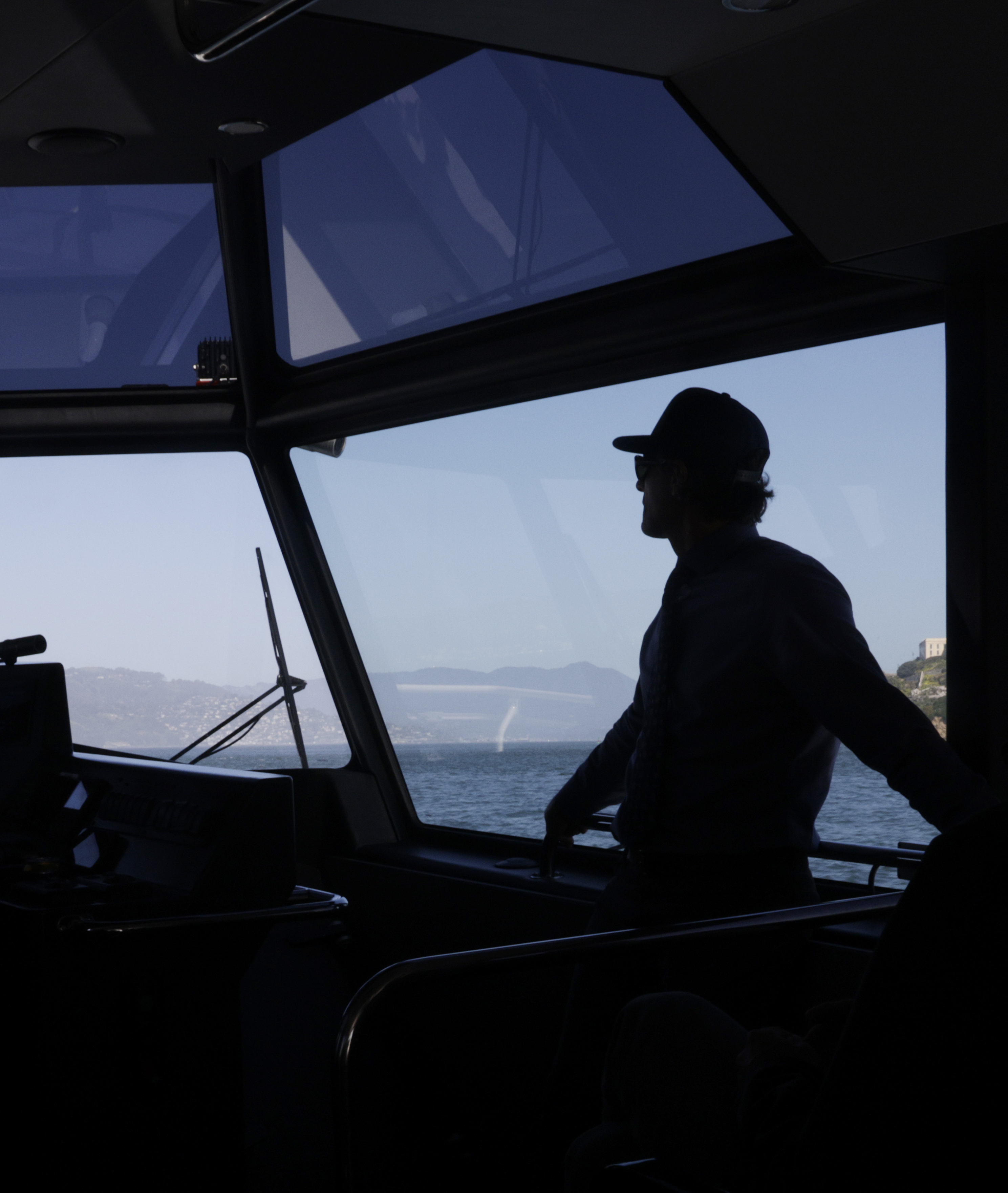 A silhouette of a person piloting a boat, with a clear view of the sea and horizon through the windows.
