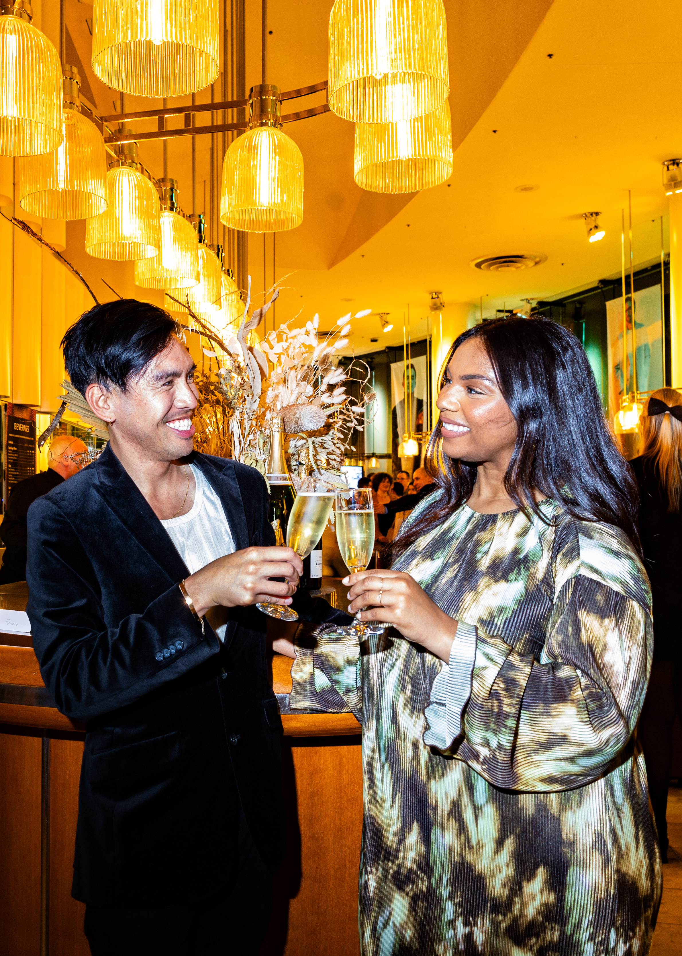 Two people are cheerfully toasting with champagne in an elegant setting with warm lighting.
