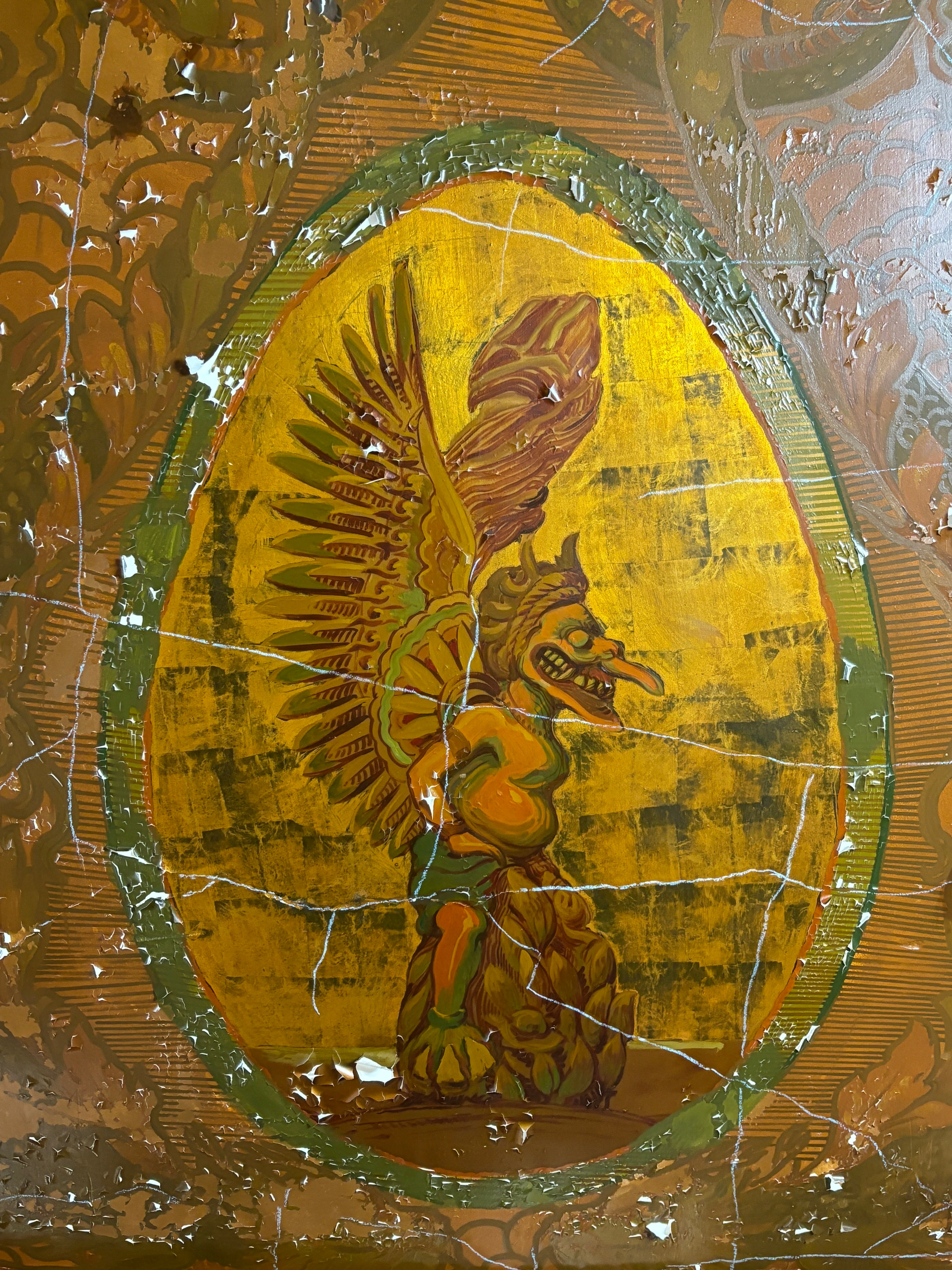a detail from a ceiling shows a winged, god-like figure in profile on a cracked and yellowed oval