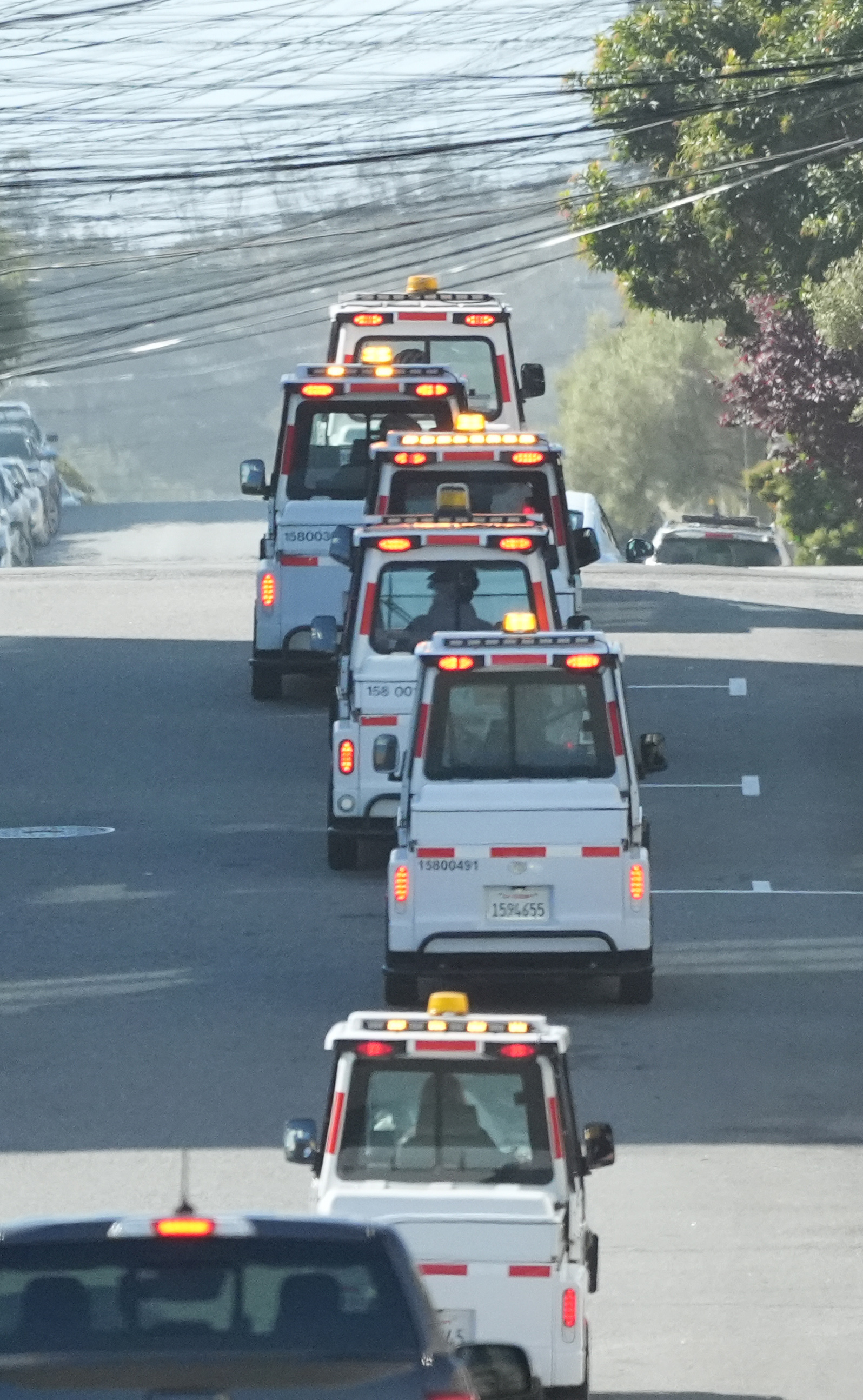 A line of parking control vehicles with flashing lights on a road.