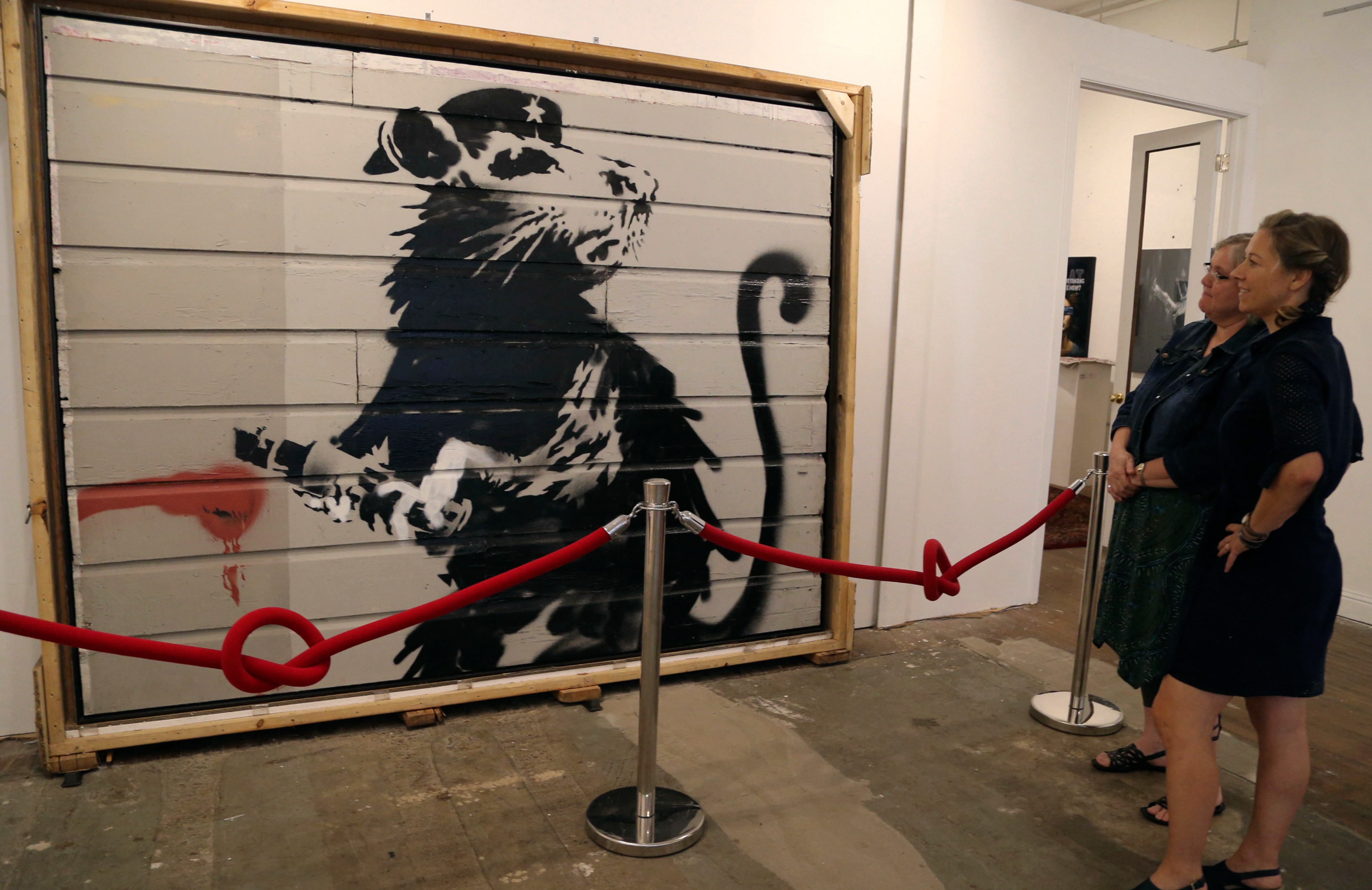 A graffiti painting of a rat is displayed in a museum.