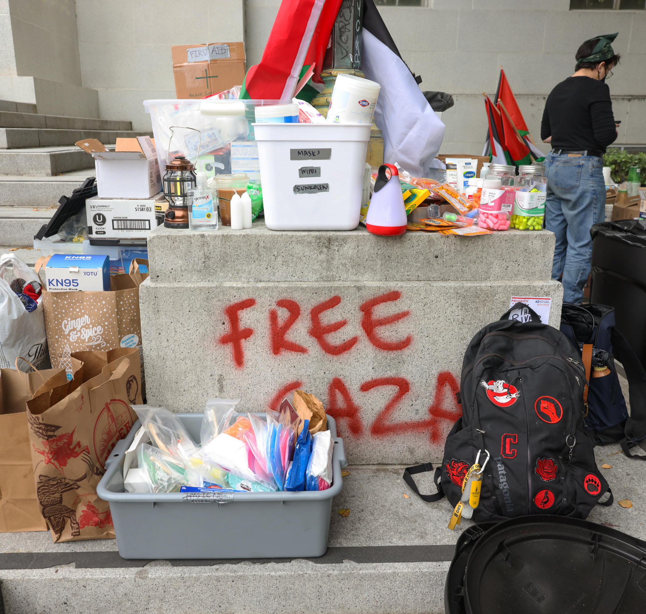 Supplies spread on steps beneath &quot;FREE GAZA&quot; graffiti; a person stands to the side.