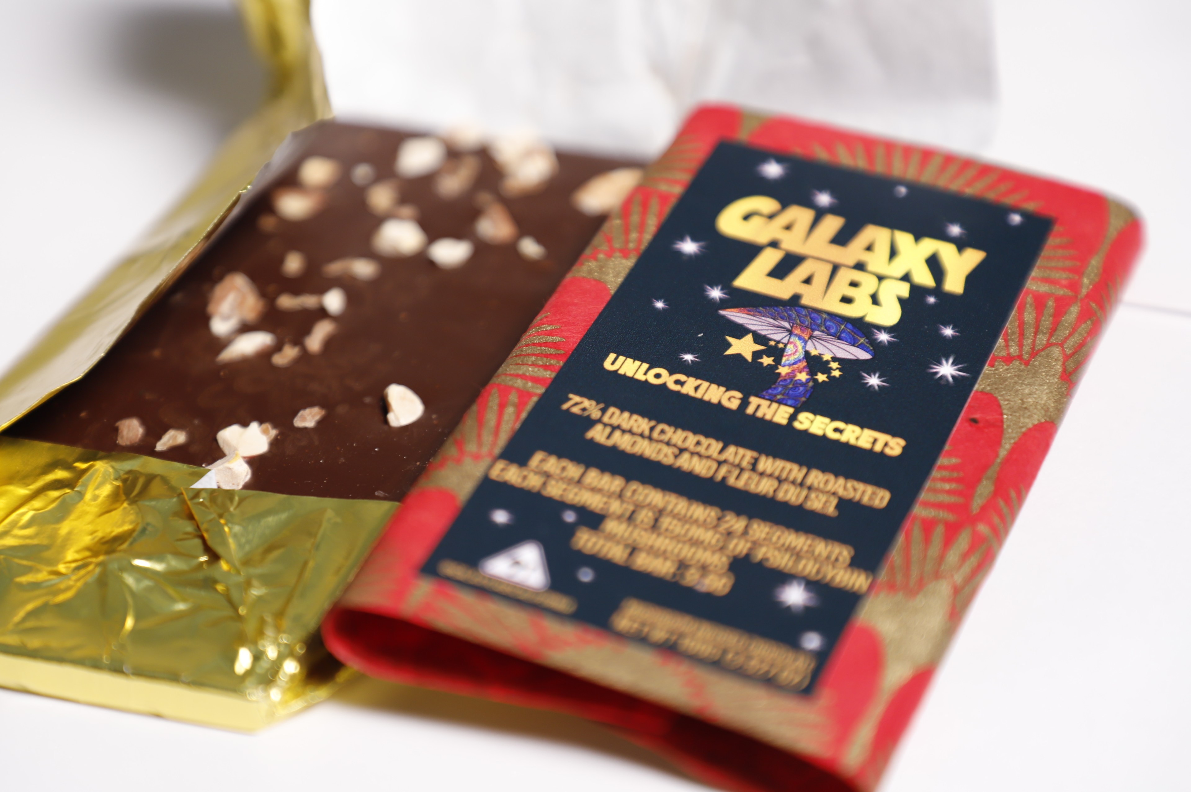 A Galaxy Labs chocolate bar of dark chocolate and almonds peeks out of gold foil wrapping.  