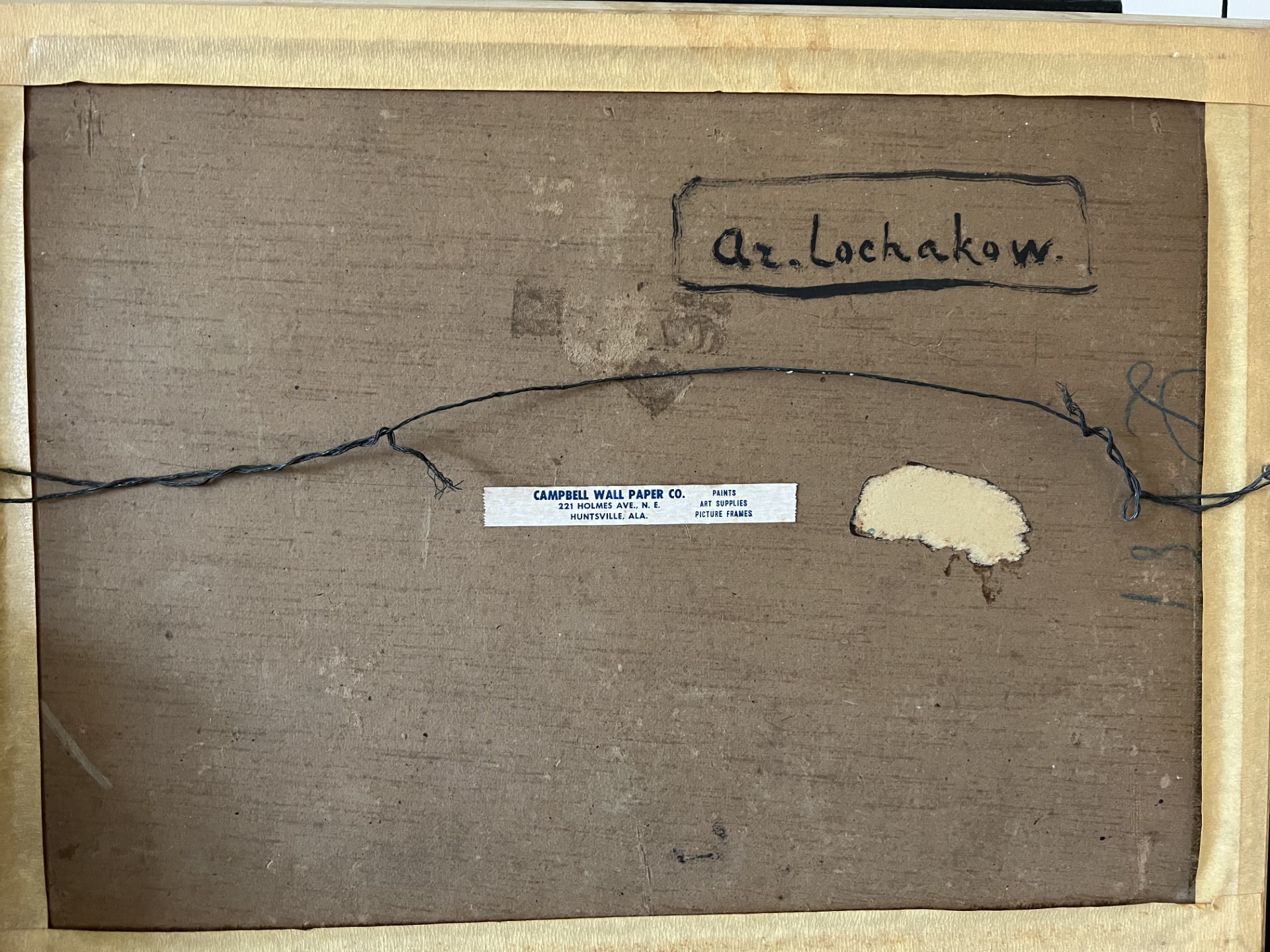 Back of a framed artwork with a frayed wire, label, and handwritten text on the top.