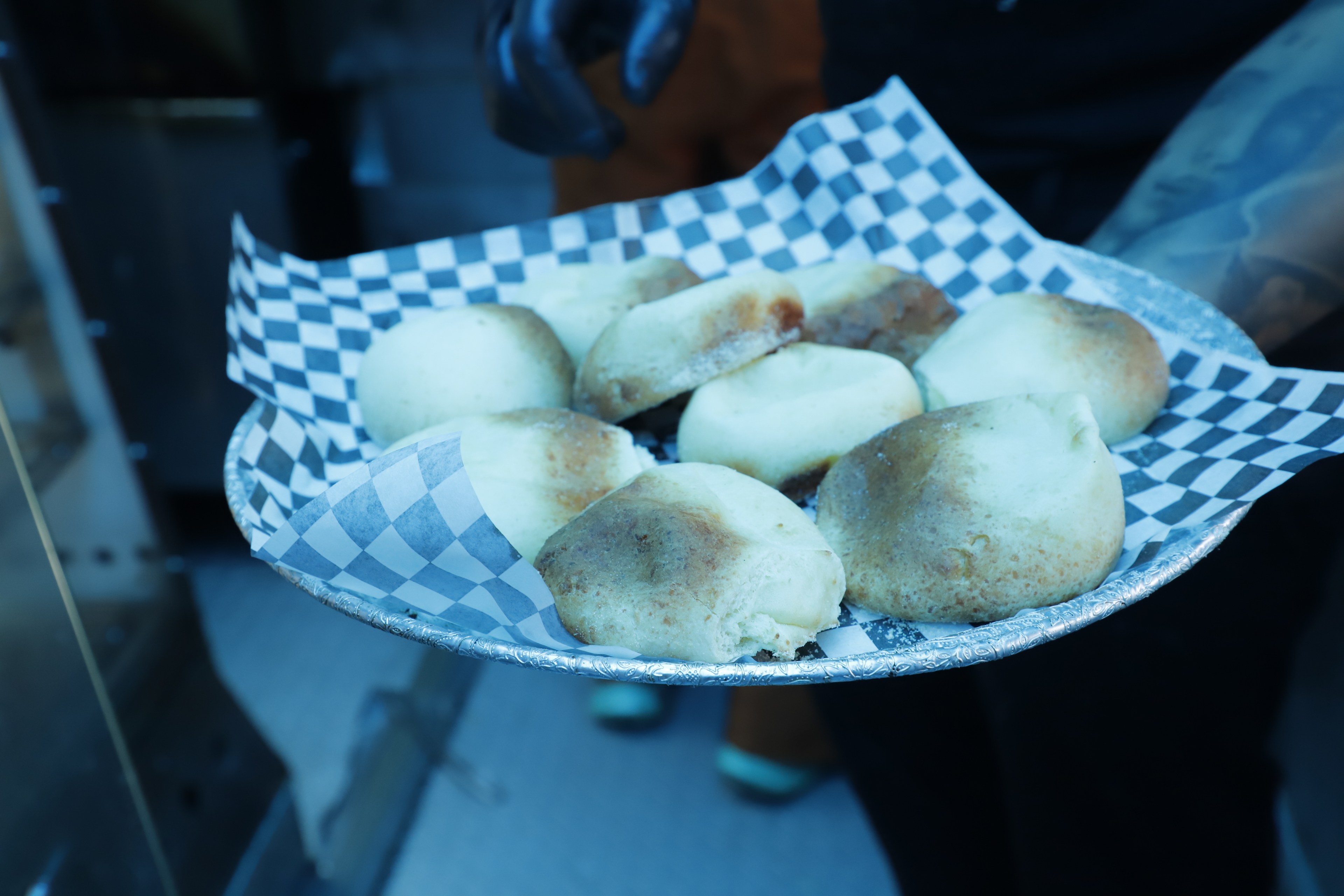 A platter of round, baked rolls on a checkered paper, held by someone in black gloves.