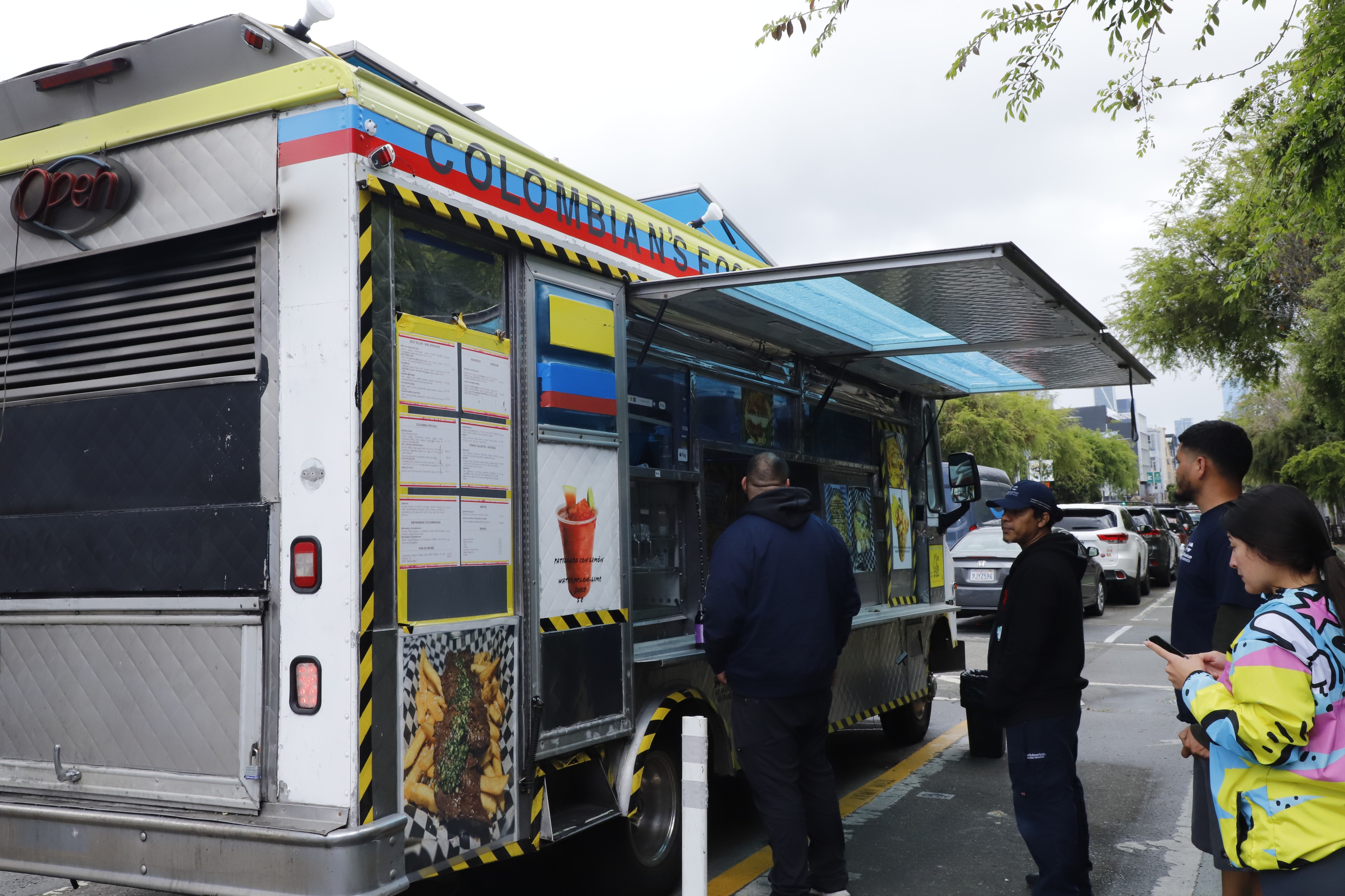 A colorful food truck with &quot;COLOMBIAN FOOD&quot; on it and people queuing to order.