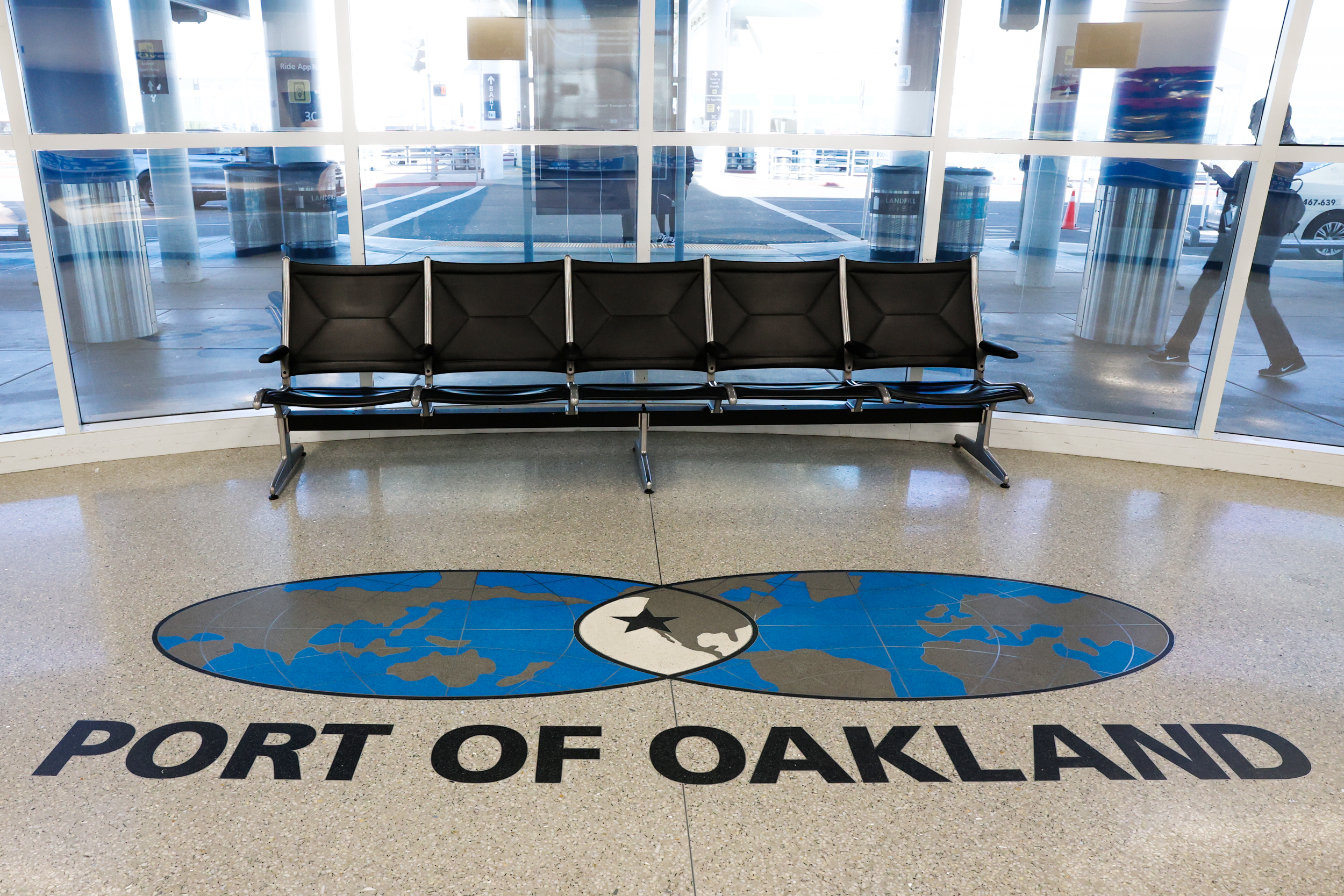 A row of black seats in a terminal with a floor emblem reading &quot;PORT OF OAKLAND&quot; featuring a globe and airplane.