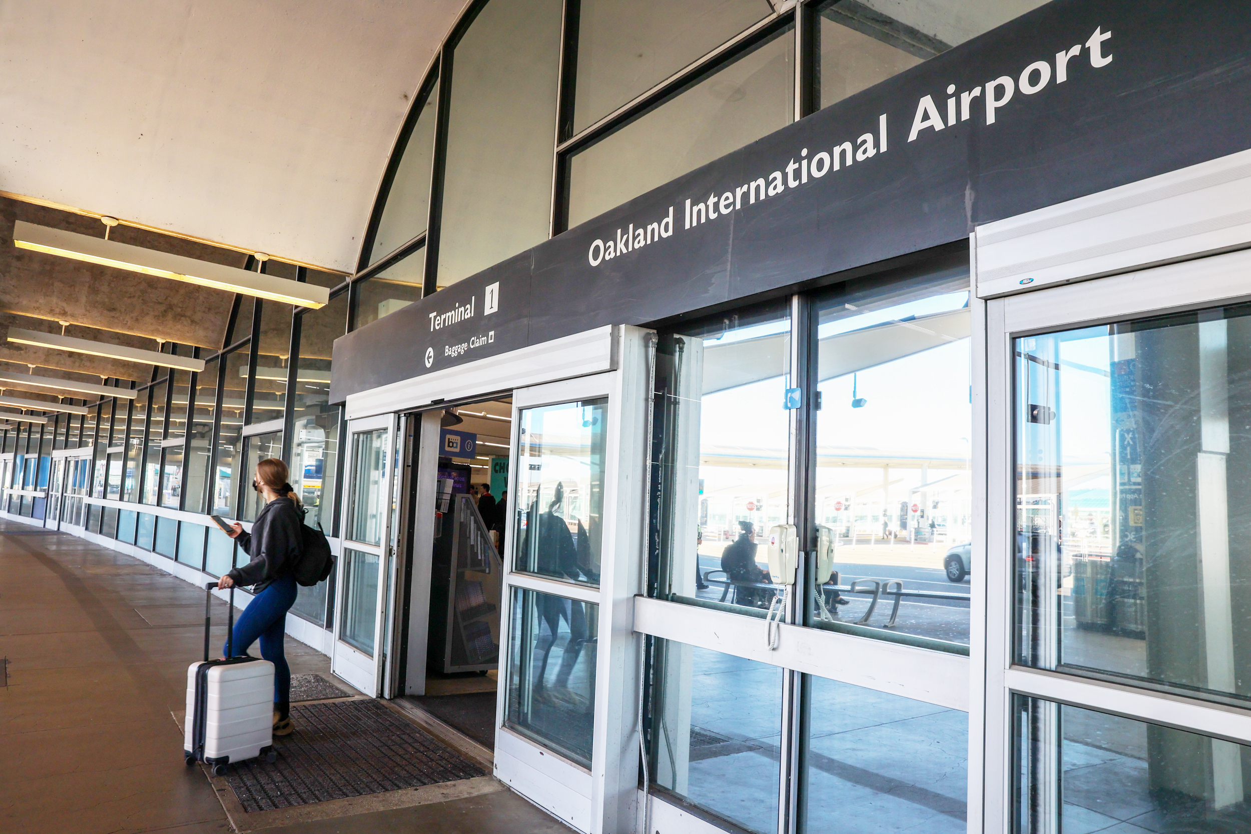 A traveler stands near a sliding door at Oakland International Airport's Terminal 1.