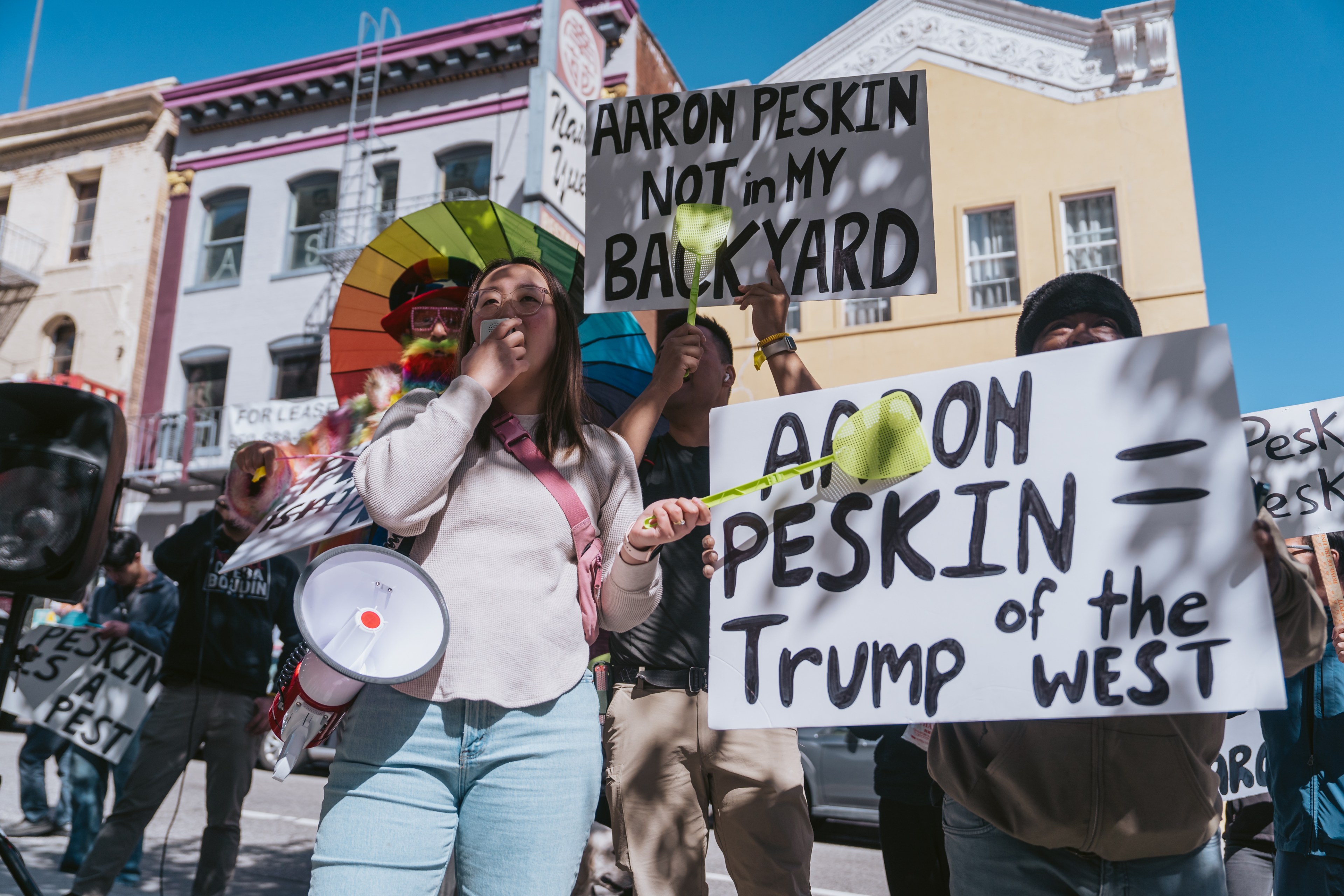 Protesters with signs that equate a person named Aaron Peskin with negativity and rebuke.